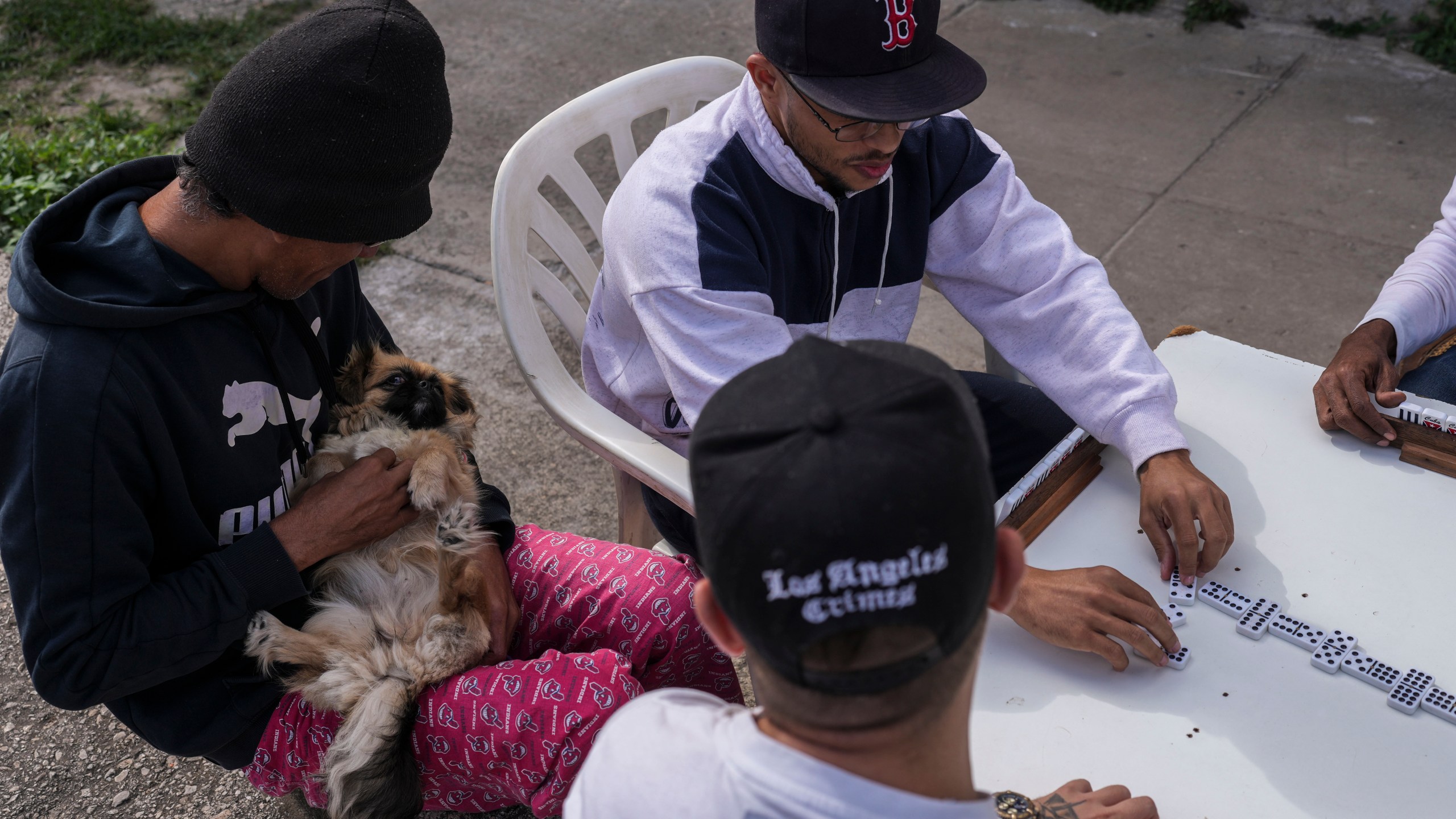 A man pets his dog as friends play dominoes outdoors during a blackout in Havana, Cuba, Wednesday, Dec. 4, 2024. (AP Photo/Ramon Espinosa)