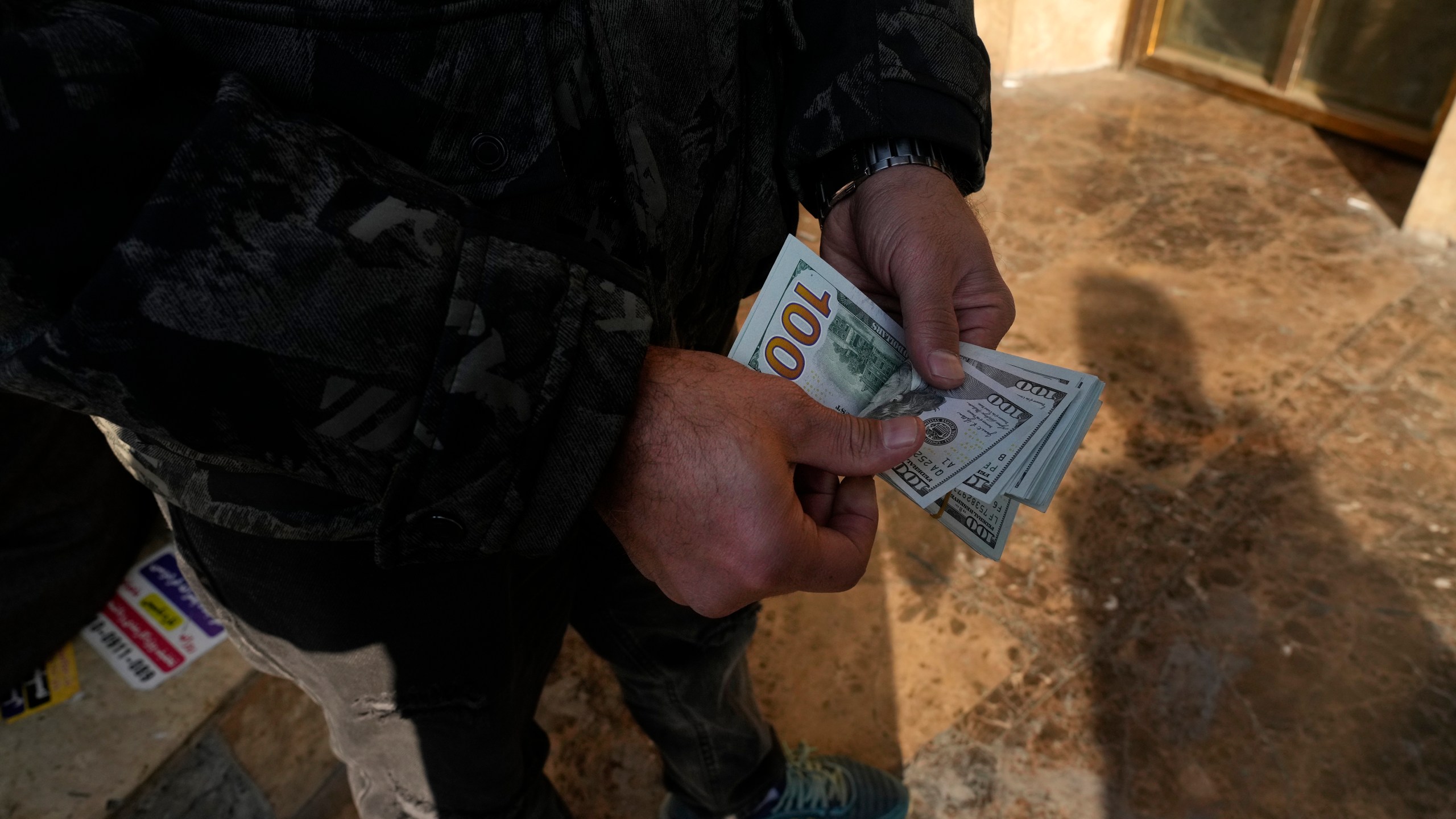 A man poses for a photo without showing his face as he counts U.S. dollars at Ferdowsi street, Tehran's go-to venue for foreign currency exchange, in downtown Tehran, Iran, Wednesday, Dec. 18, 2024. (AP Photo/Vahid Salemi)