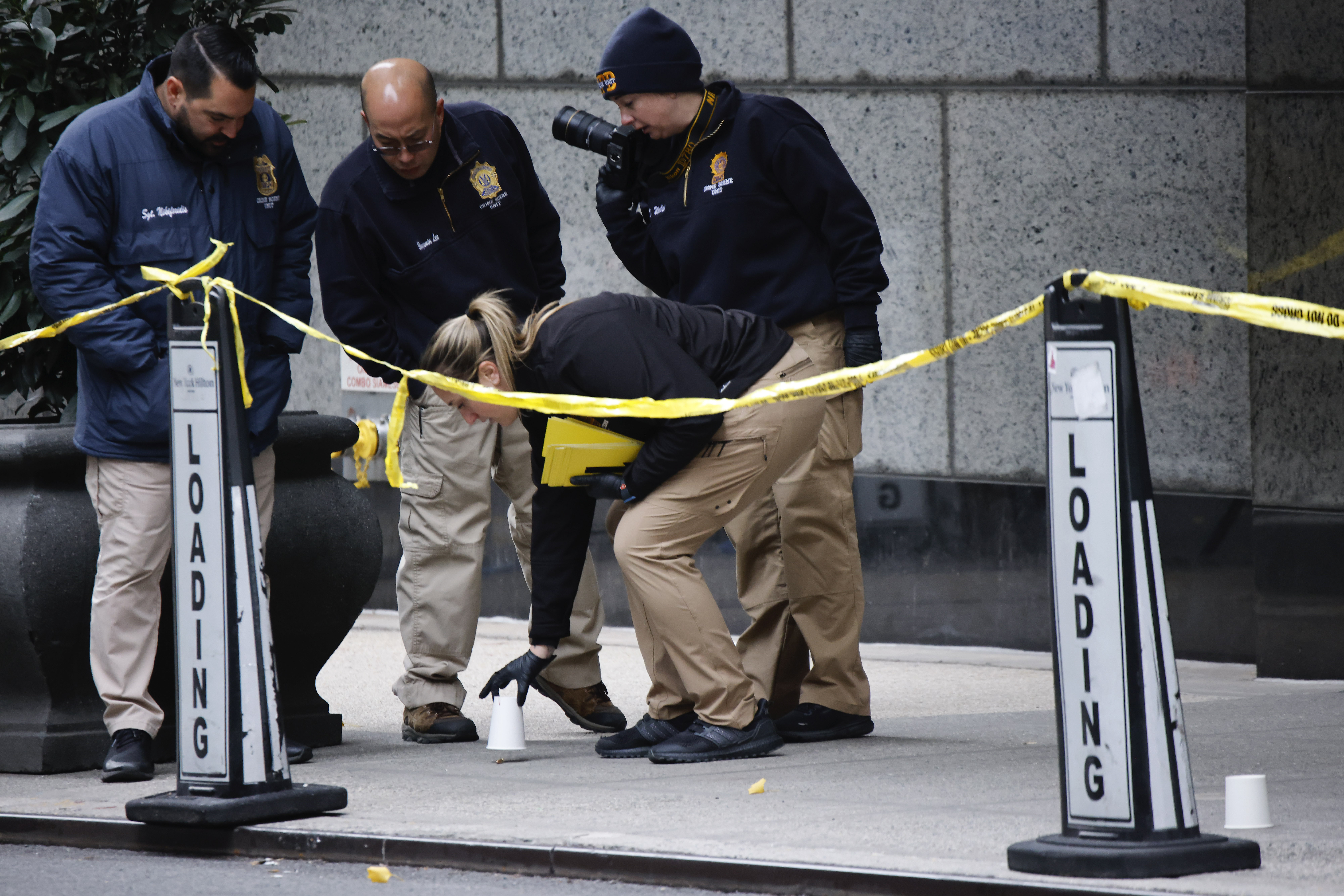 Members of the New York police crime scene unit pick up cups marking the spots where bullets lie as they investigate the scene outside the Hilton Hotel in midtown Manhattan where Brian Thompson, the CEO of UnitedHealthcare, was fatally shot Wednesday, Dec. 4, 2024, in New York. (AP Photo/Stefan Jeremiah)