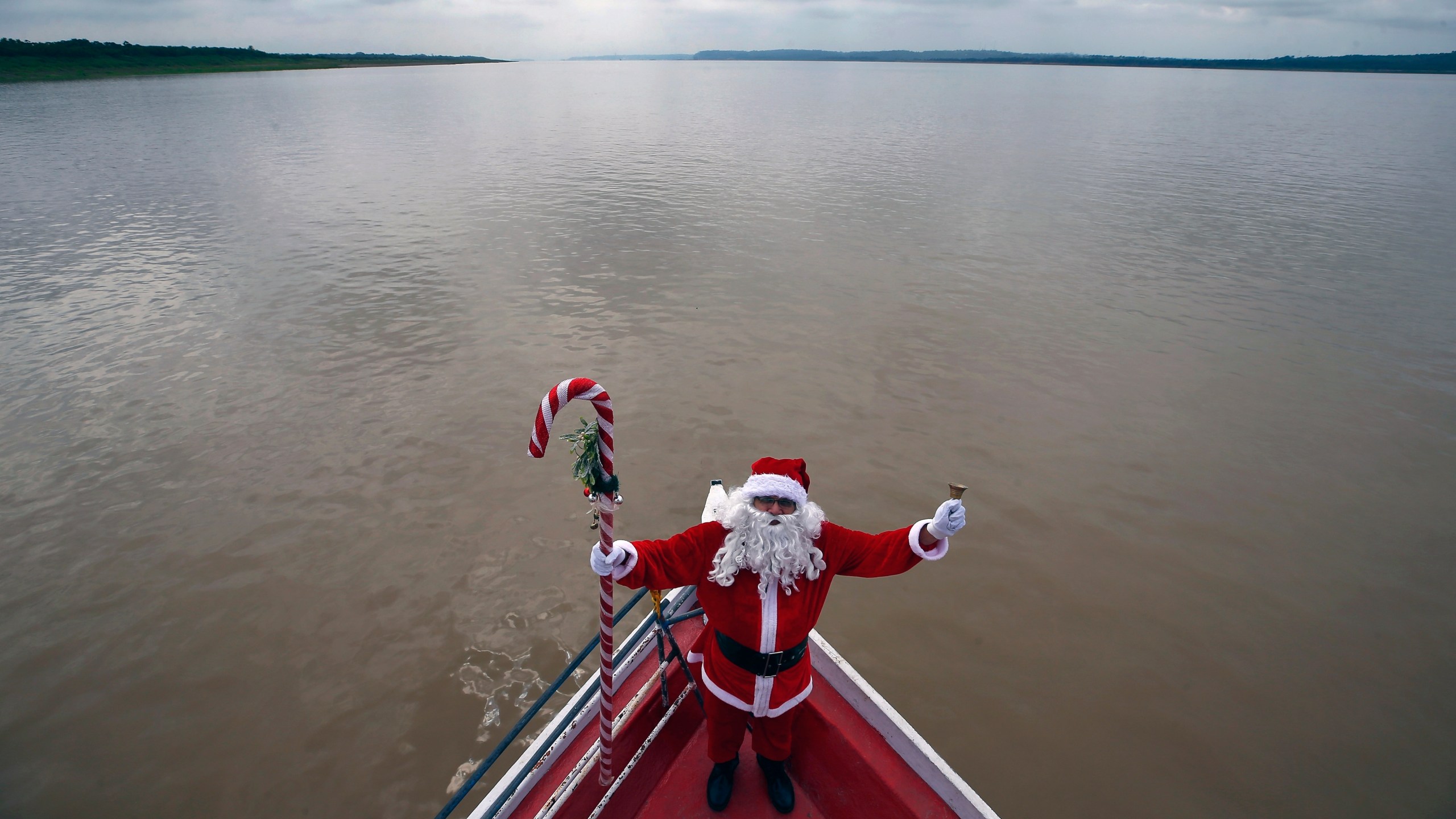 FILE - Jorge Barroso, dressed as Santa Claus, stands on his boat while sailing to visit a community along the jungle shoreline to give out presents to children in the Amazon basin, near Careiro da Varzea, Amazonas state, Brazil, Saturday, Dec. 16, 2023. (AP Photo/Edmar Barros, File)