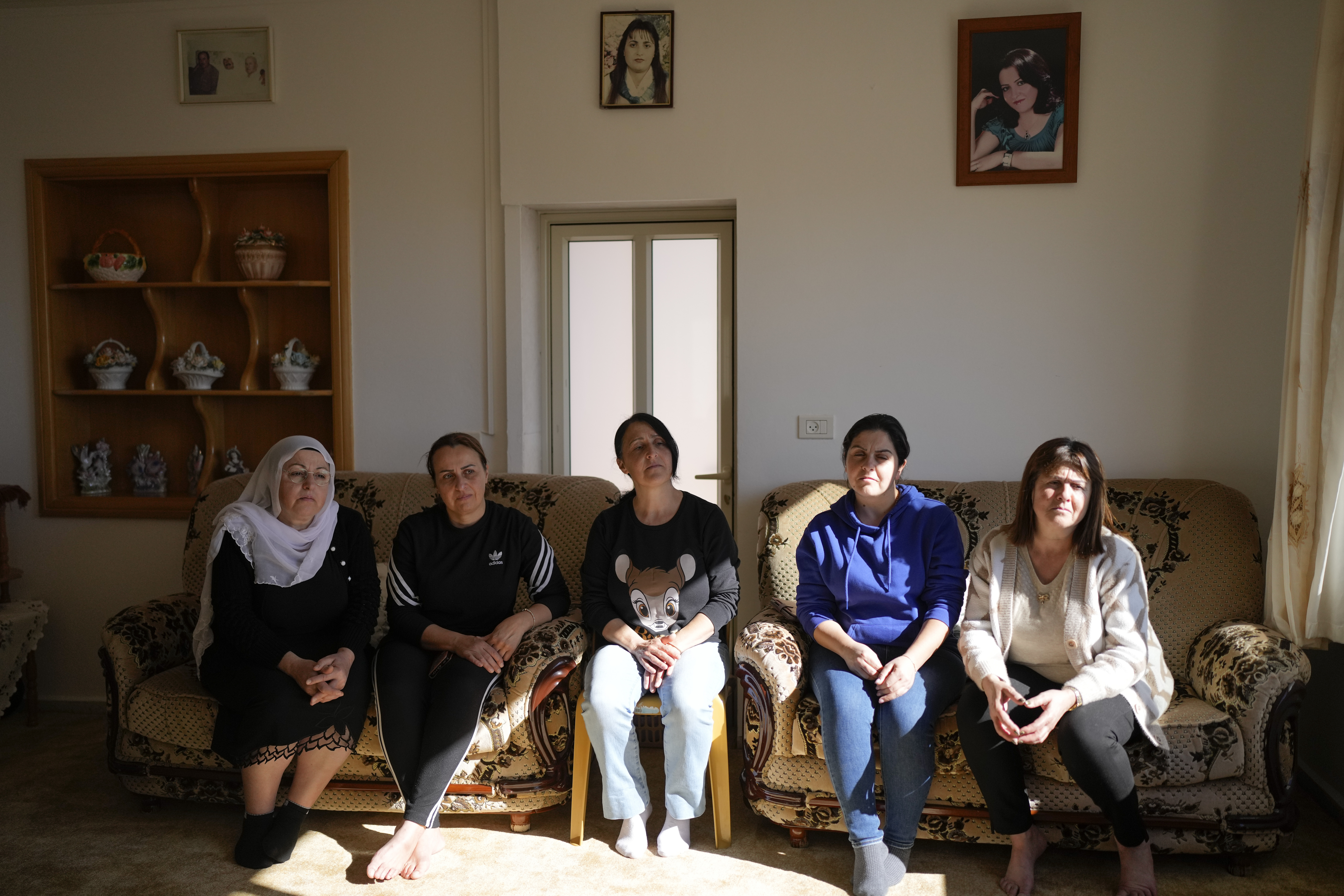 Five of six Safadi sisters sit on a couch under a portrait of their sister, Sawsan, who lives inside the buffer zone near the "Alpha Line" that separates the Israeli-controlled Golan Heights from Syria, in the town of Majdal Shams, Wednesday, Dec. 18, 2024. (AP Photo/Matias Delacroix)