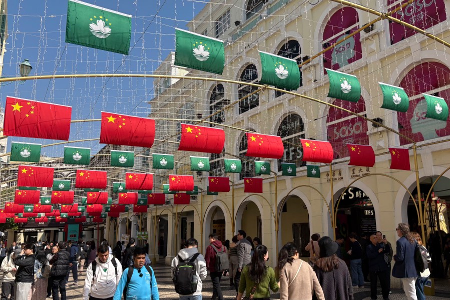 Tourists walk past a street decorated with Chinese national flags and Macao regional flags in Macao on Dec. 13, 2024. (AP Photo/Kanis Leung)