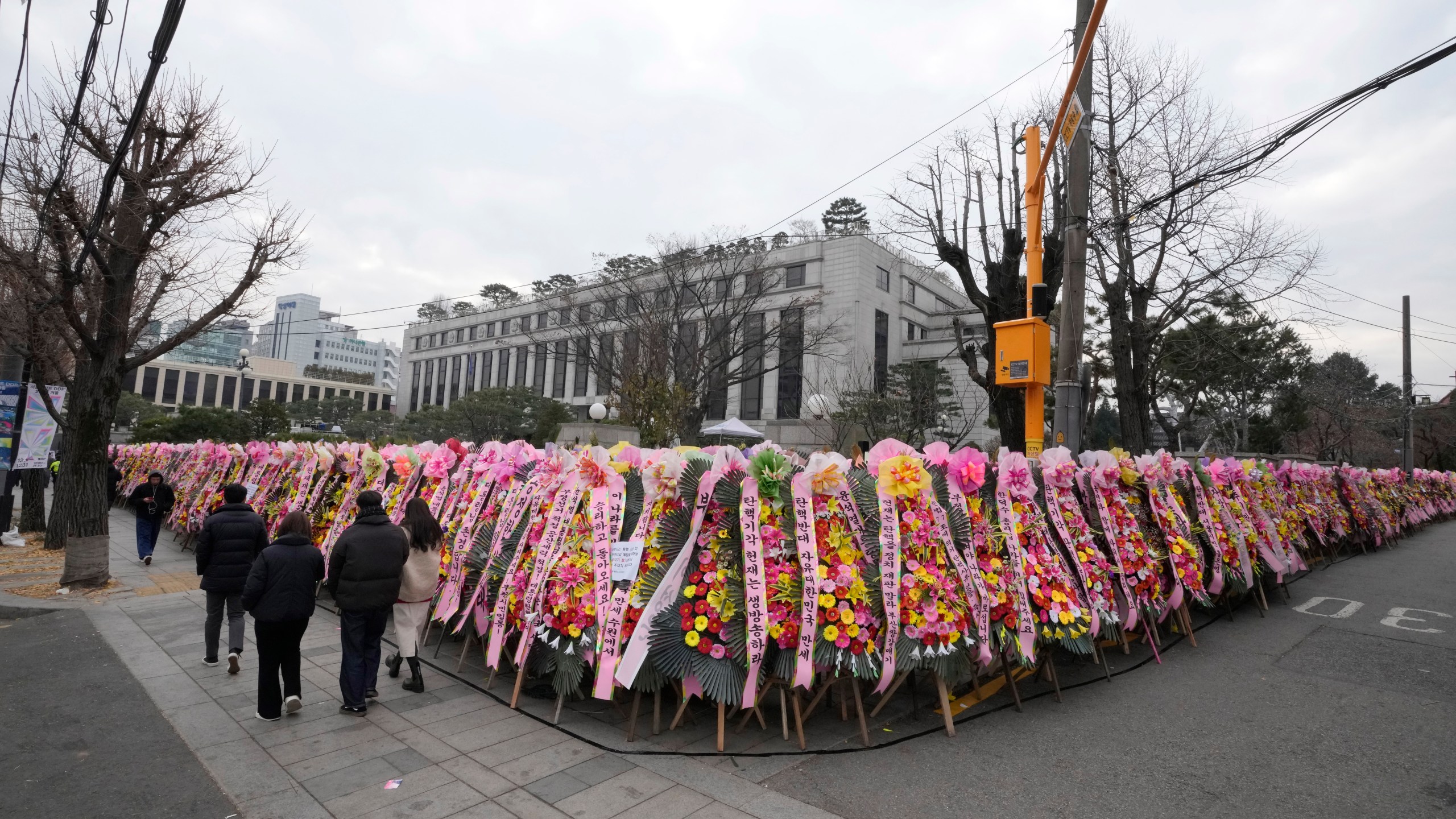 People walk past wreaths sent by supporters of impeached South Korean President Yoon Suk Yeol outside of the Constitutional Court in Seoul, South Korea, Friday, Dec. 20, 2024. (AP Photo/Ahn Young-joon)