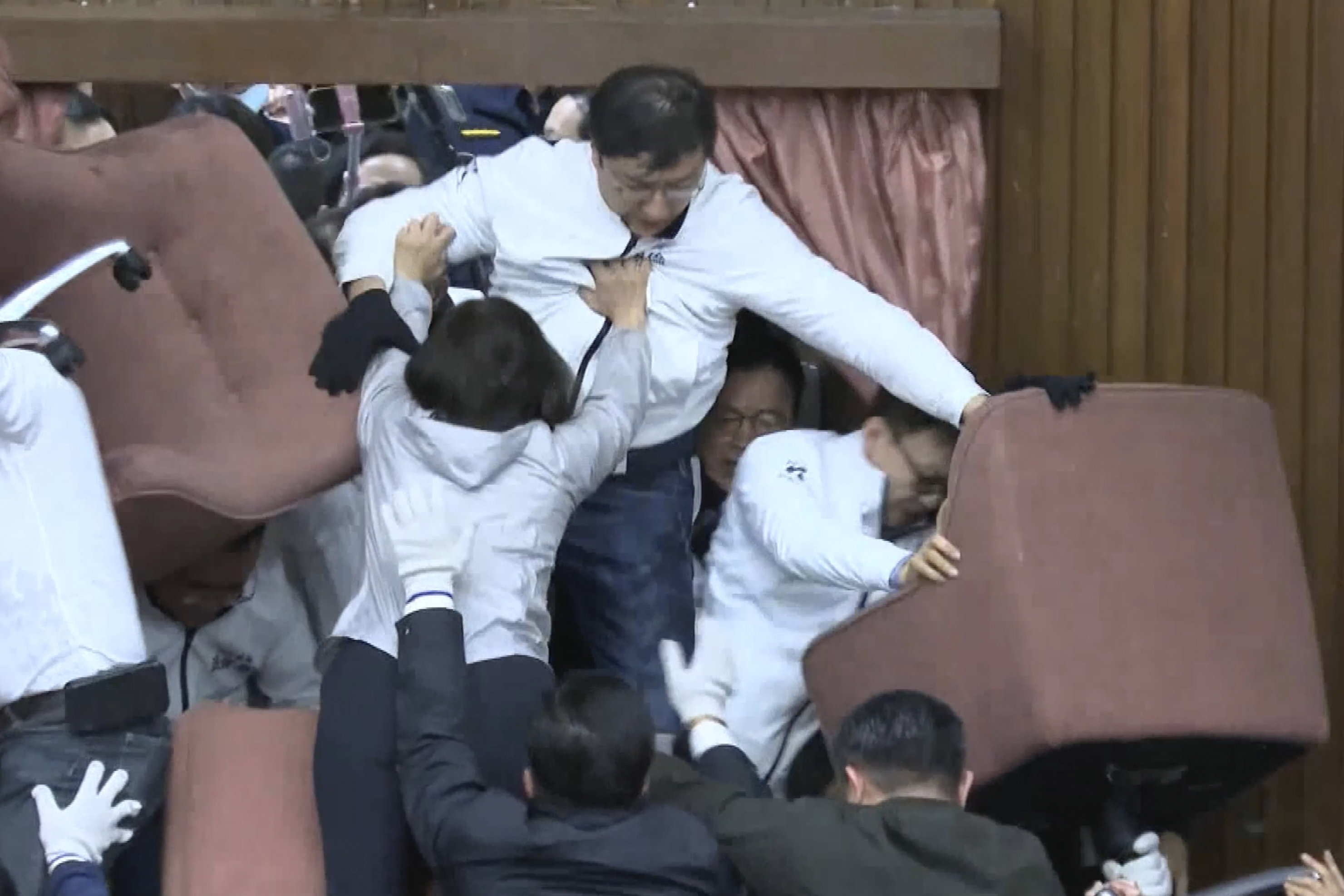 In this image made from video by Taiwan's EBC, lawmakers from the Democratic Progressive Party use chairs to block the entrance as members of the Nationalist Party, or Kuomintang, try to break into the Legislature in Taipei, Taiwan on Friday, Dec 20, 2024. (EBC via AP )