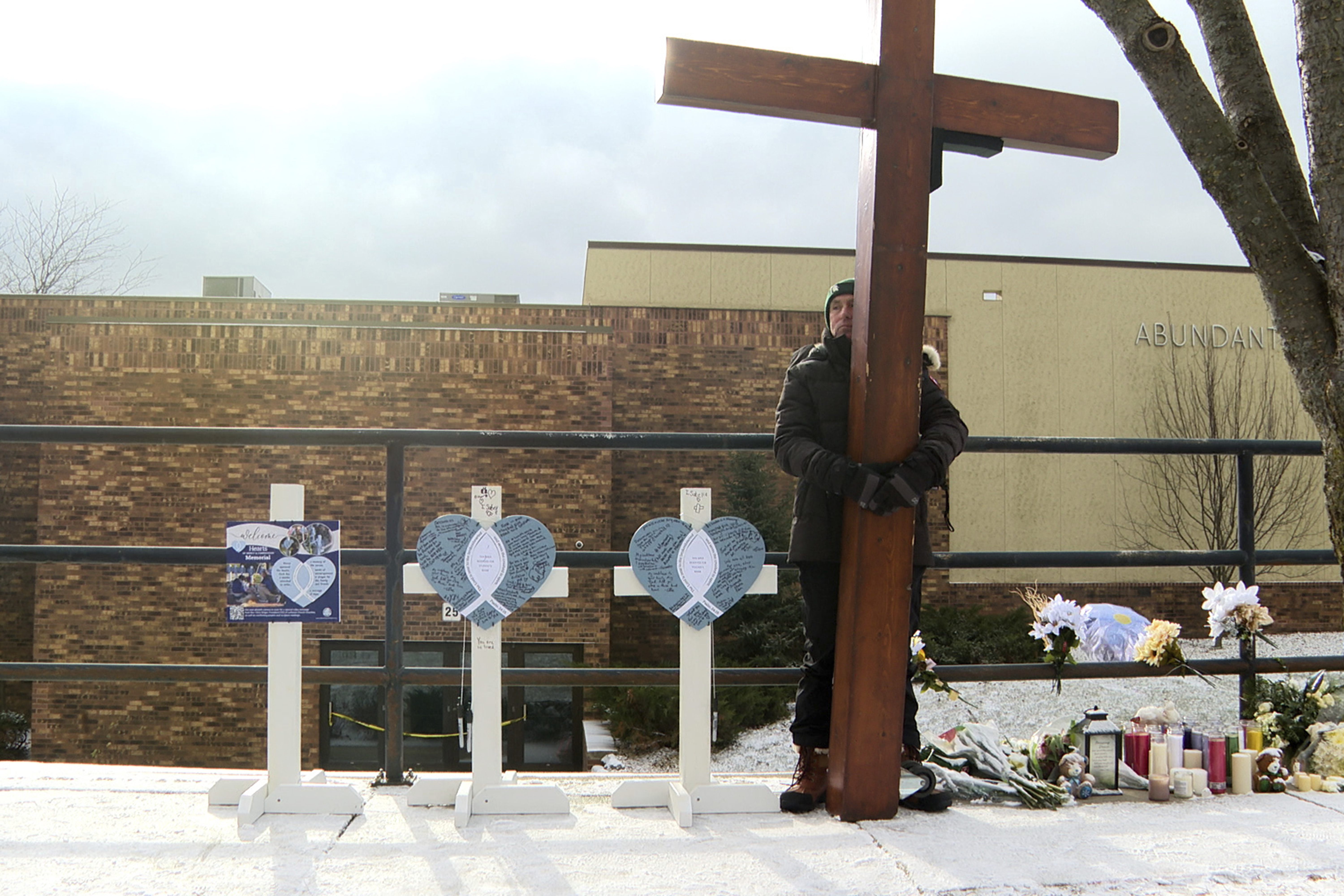 Dan Beazley stands with the homemade cross he brought from Michigan for victims of a shooting at Abundant Life Christian School Wednesday, Dec. 18, 2024, in Madison, Wis. (AP Photo/Mark Vancleave)