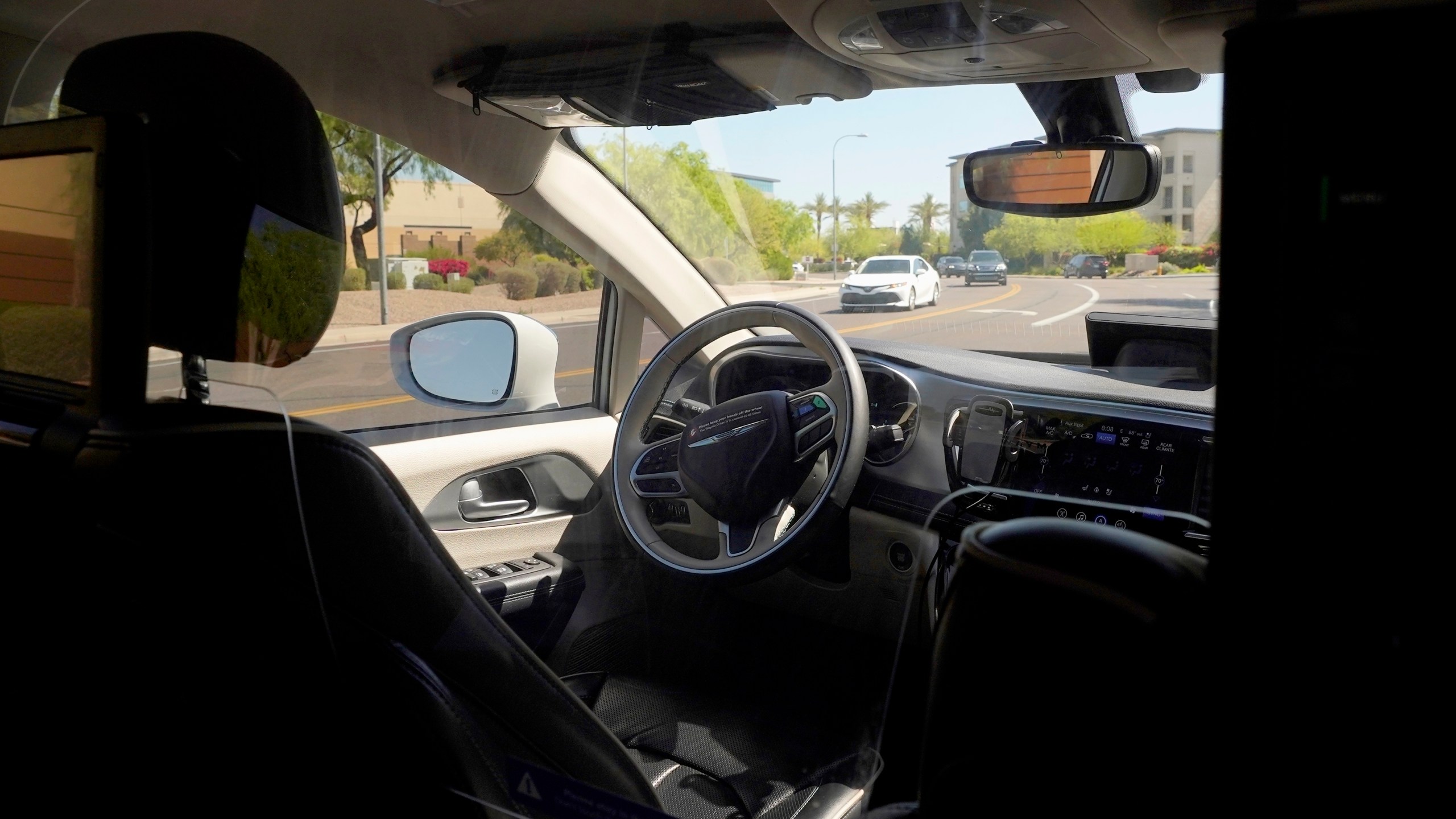 FILE - A Waymo minivan moves along a city street as an empty driver's seat and a moving steering wheel drive passengers during an autonomous vehicle ride, on April 7, 2021, in Chandler, Ariz. (AP Photo/Ross D. Franklin, File)