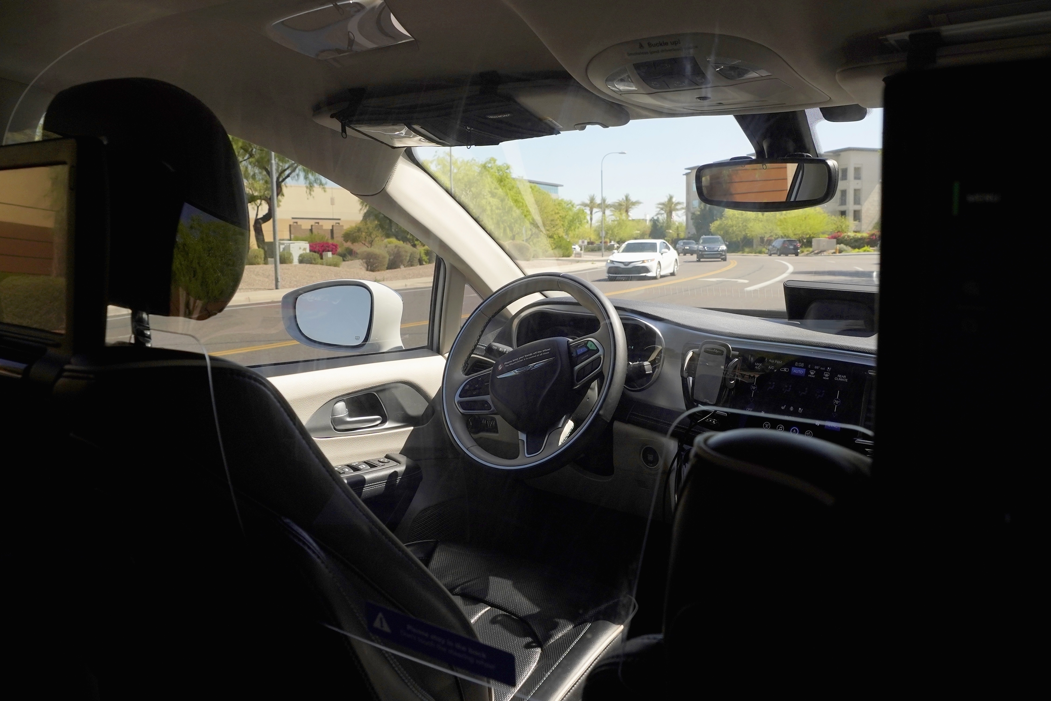 FILE - A Waymo minivan moves along a city street as an empty driver's seat and a moving steering wheel drive passengers during an autonomous vehicle ride, on April 7, 2021, in Chandler, Ariz. (AP Photo/Ross D. Franklin, File)