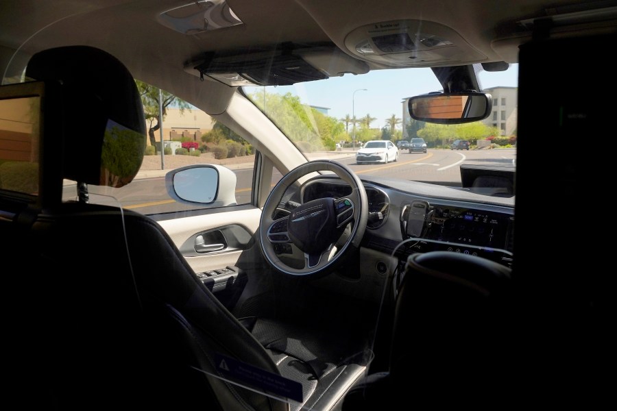 FILE - A Waymo minivan moves along a city street as an empty driver's seat and a moving steering wheel drive passengers during an autonomous vehicle ride, on April 7, 2021, in Chandler, Ariz. (AP Photo/Ross D. Franklin, File)