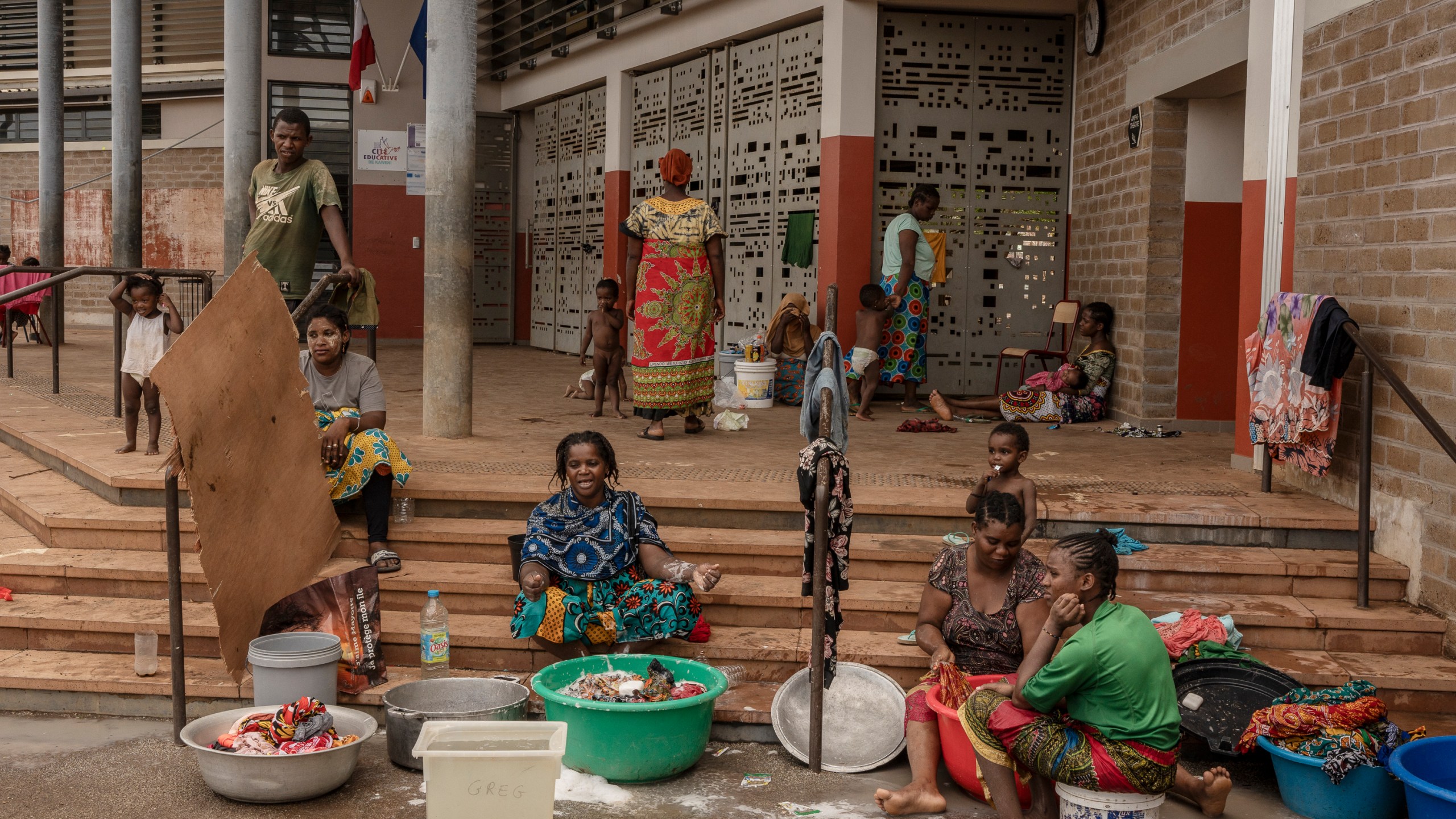 Women wash clothes after a short rain filled their pots with water, at the Lycée des Lumières where they found shelter after losing their homes, in Mamoudzou, Mayotte, Thursday, Dec. 19, 2024 . (AP Photo/Adrienne Surprenant)