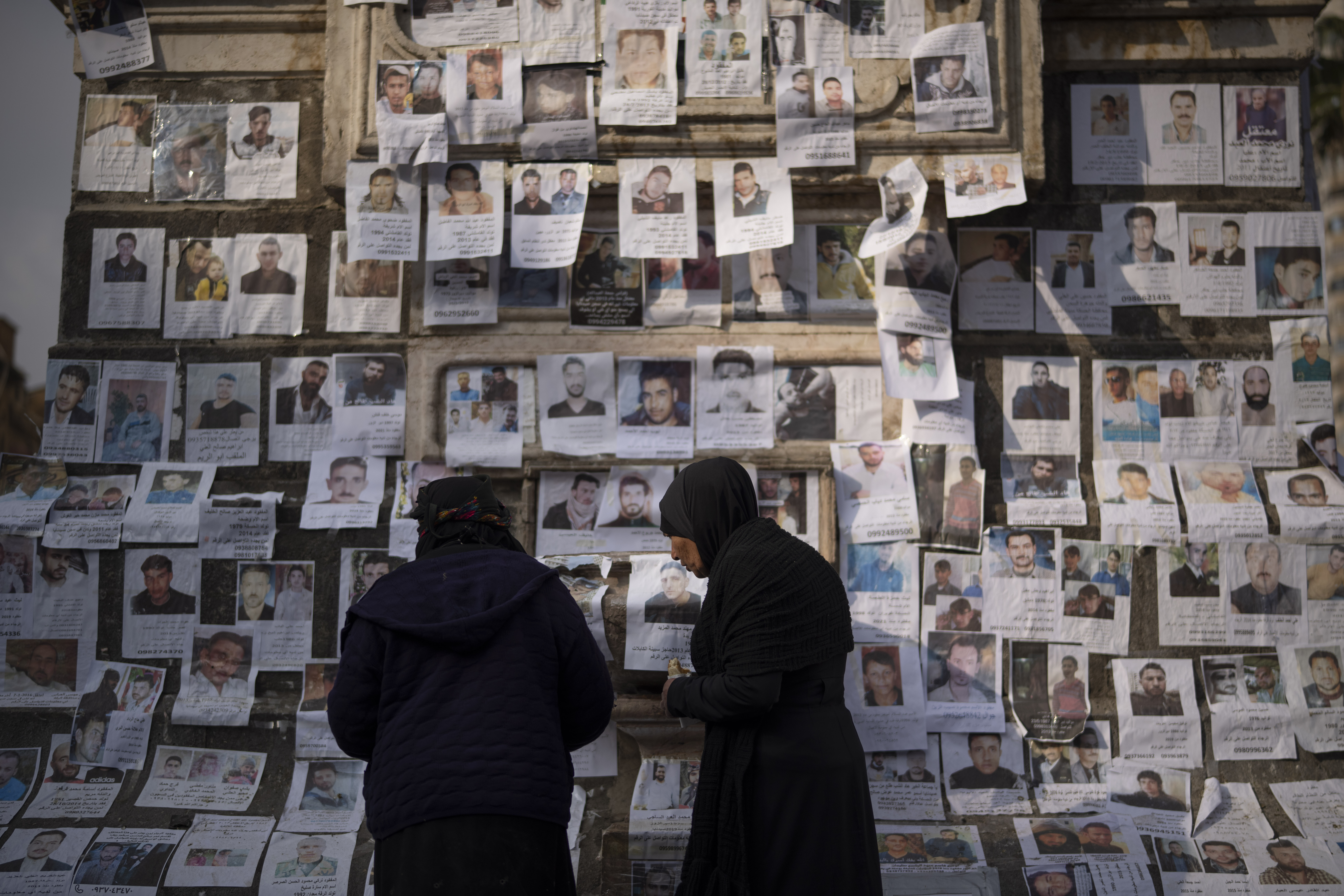 Women look at photos of people reported to be missing by members of ousted Syrian President Bashar Assad's army, or a pro-government militia, in the Marjeh square in Damascus, Syria, Sunday, Dec. 22, 2024. (AP Photo/Leo Correa)