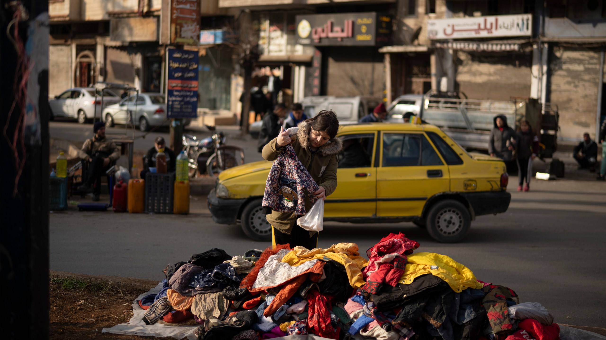 A women looks at second hand clothes displayed on a street for sale near an Alawite neighbourhood, in Homs, Syria, Thursday, Dec. 26, 2024. (AP Photo/Leo Correa)