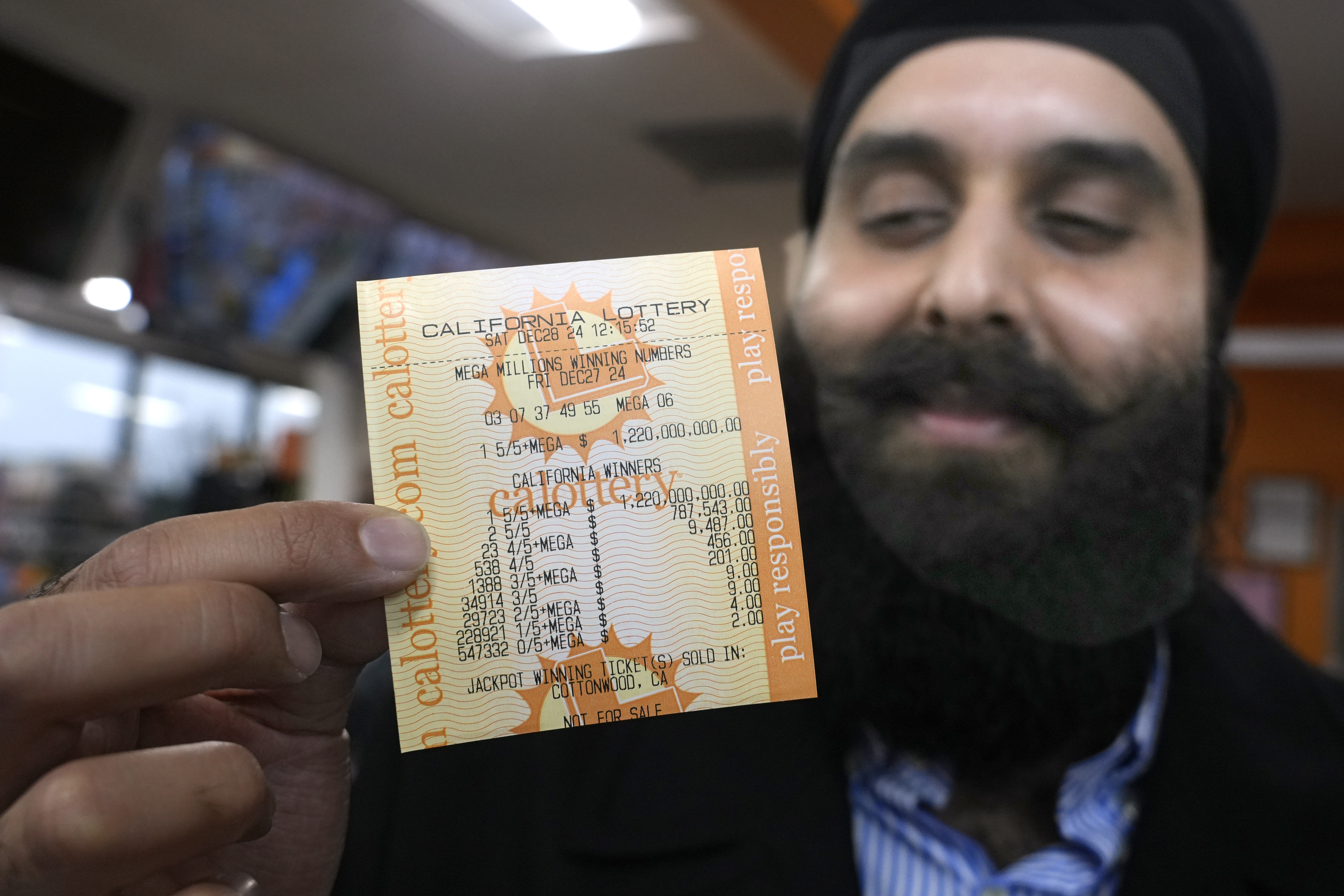 Ishar Gill holds up a copy of the Mega Millions lotto ticket worth an estimated $1.22 billion at his family's store in Cottonwood, Calif., Saturday, Dec. 28, 2024. After three months without anyone winning the top prize in the lottery, the ticket with the winning numbers was drawn Friday night.(AP Photo/Rich Pedroncelli).