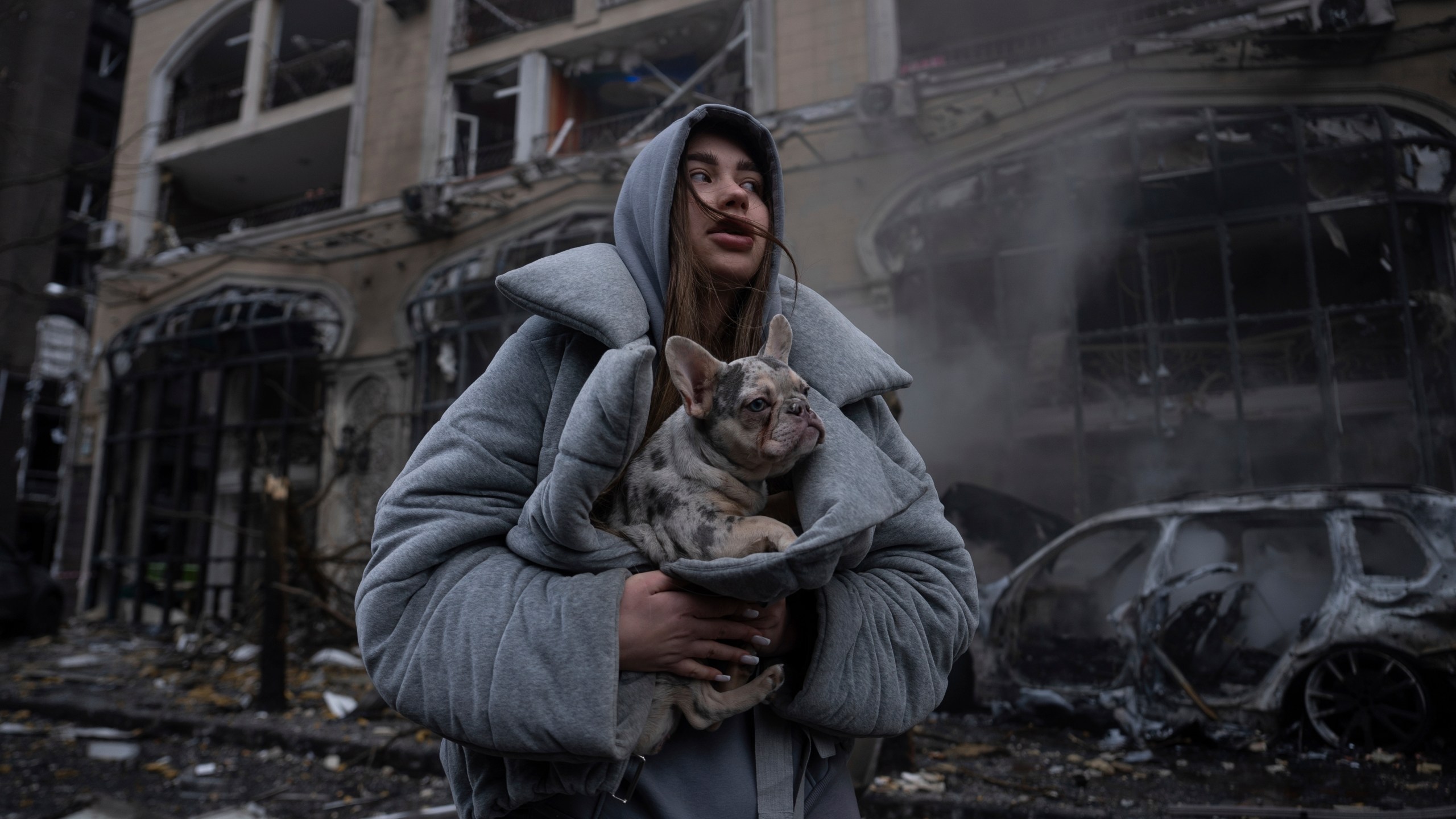 Ivanna, warms her dog in front of a destroyed burning car after a recent Russian attack in Kyiv, Ukraine, Friday, Dec. 20, 2024. (AP Photo/Alex Babenko)