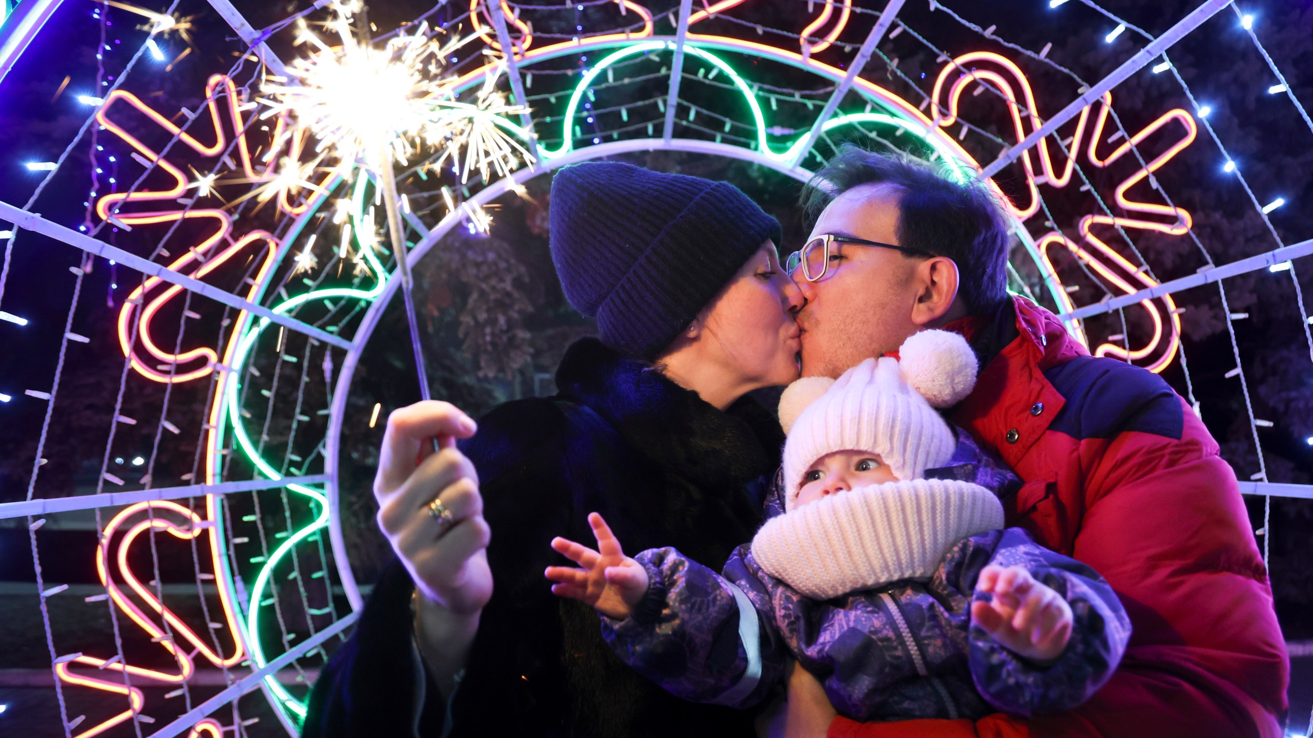 A couple kisses as they walk with their child in a square decorated for Christmas and the New Year festivities in Donetsk in Russian-controlled Donetsk region, eastern Ukraine, Tuesday, Dec. 31, 2024. (AP Photo/Alexei Alexandrov)