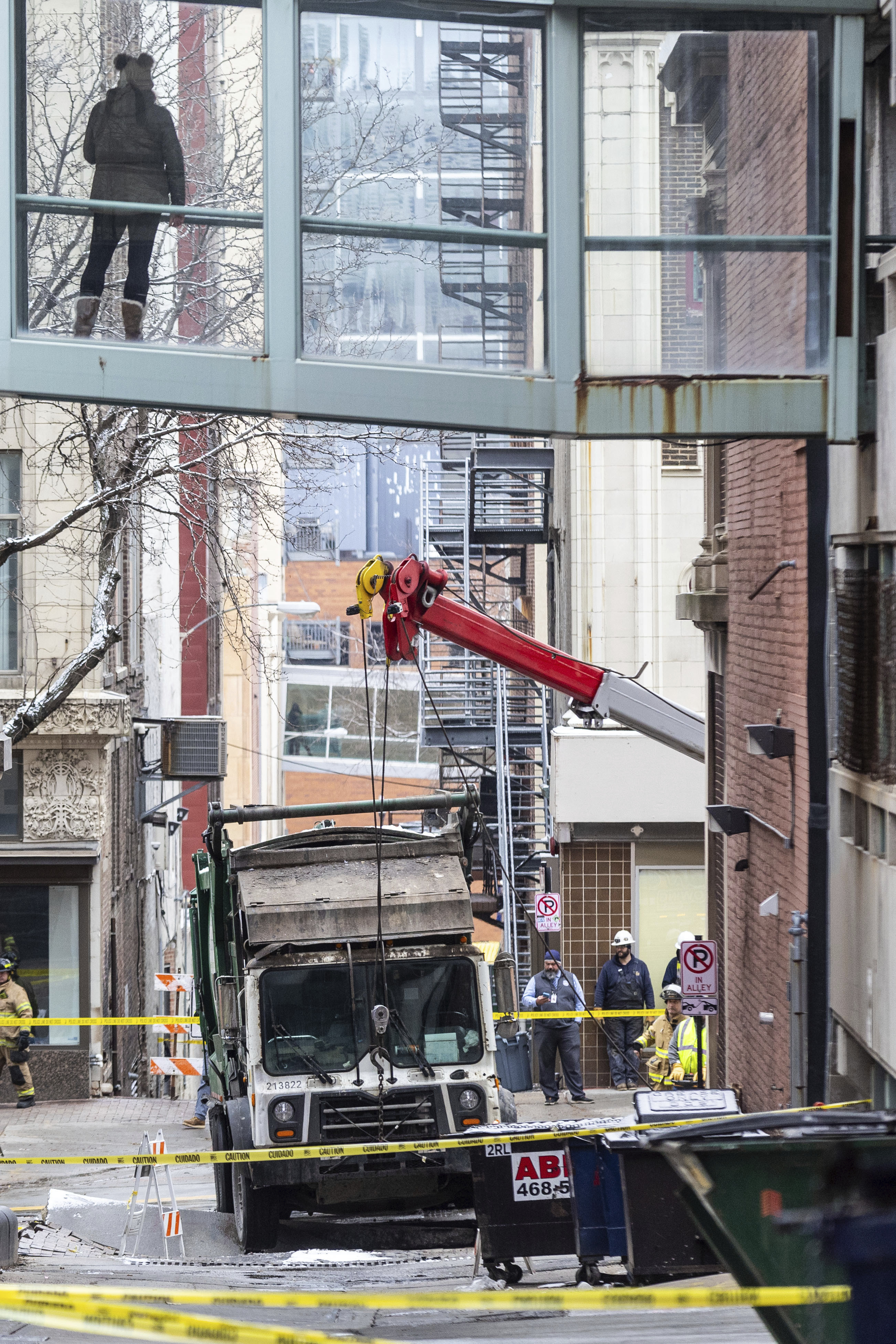 A person watches from a skywalk as workers use a crane to lift a garbage truck that got stuck in a sinkhole in downtown Omaha, Neb., Thursday, Jan. 2, 2025. (Chris Machian/Omaha World-Herald via AP)