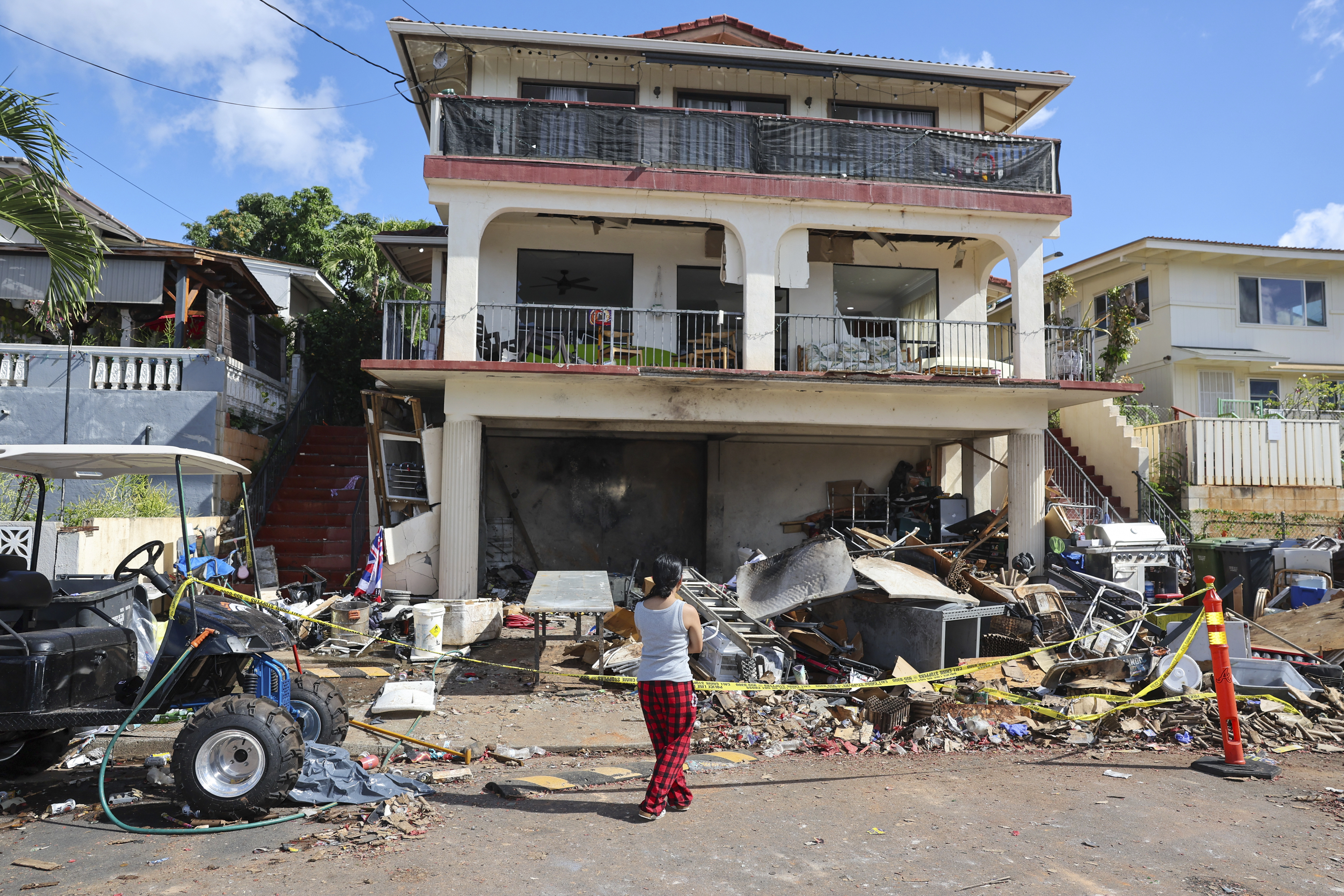 A woman stands in front of the home where a New Year's Eve fireworks explosion killed and injured people, Wednesday, Jan. 1, 2025, in Honolulu. (AP Photo/Marco Garcia)