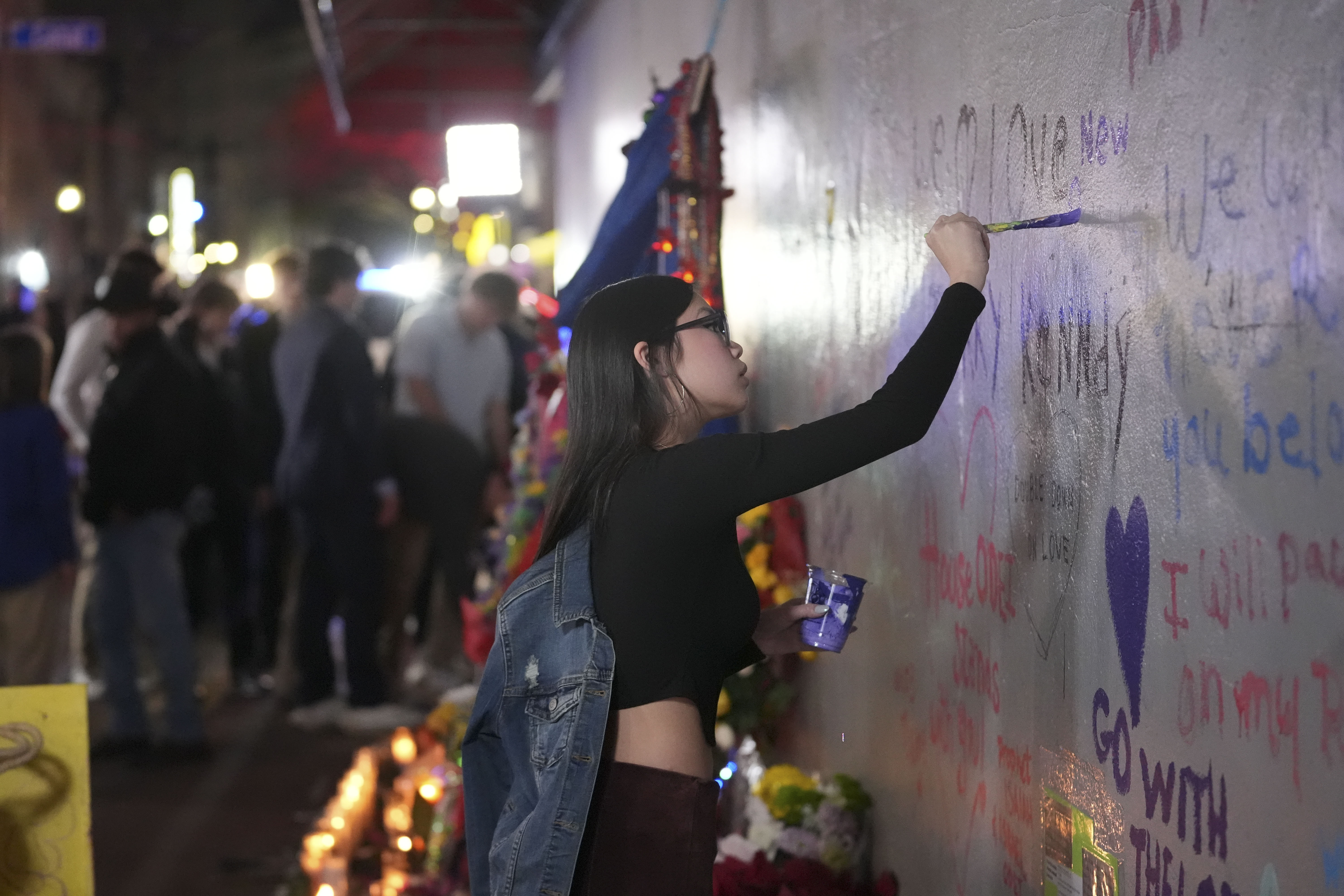 A woman paints a heart as friends of Kareem Badawi, a victim of the deadly truck attack on New Year's Day in New Orleans, visit a memorial for victims after attending his funeral, Friday, Jan. 3, 2025. (AP Photo/Gerald Herbert)