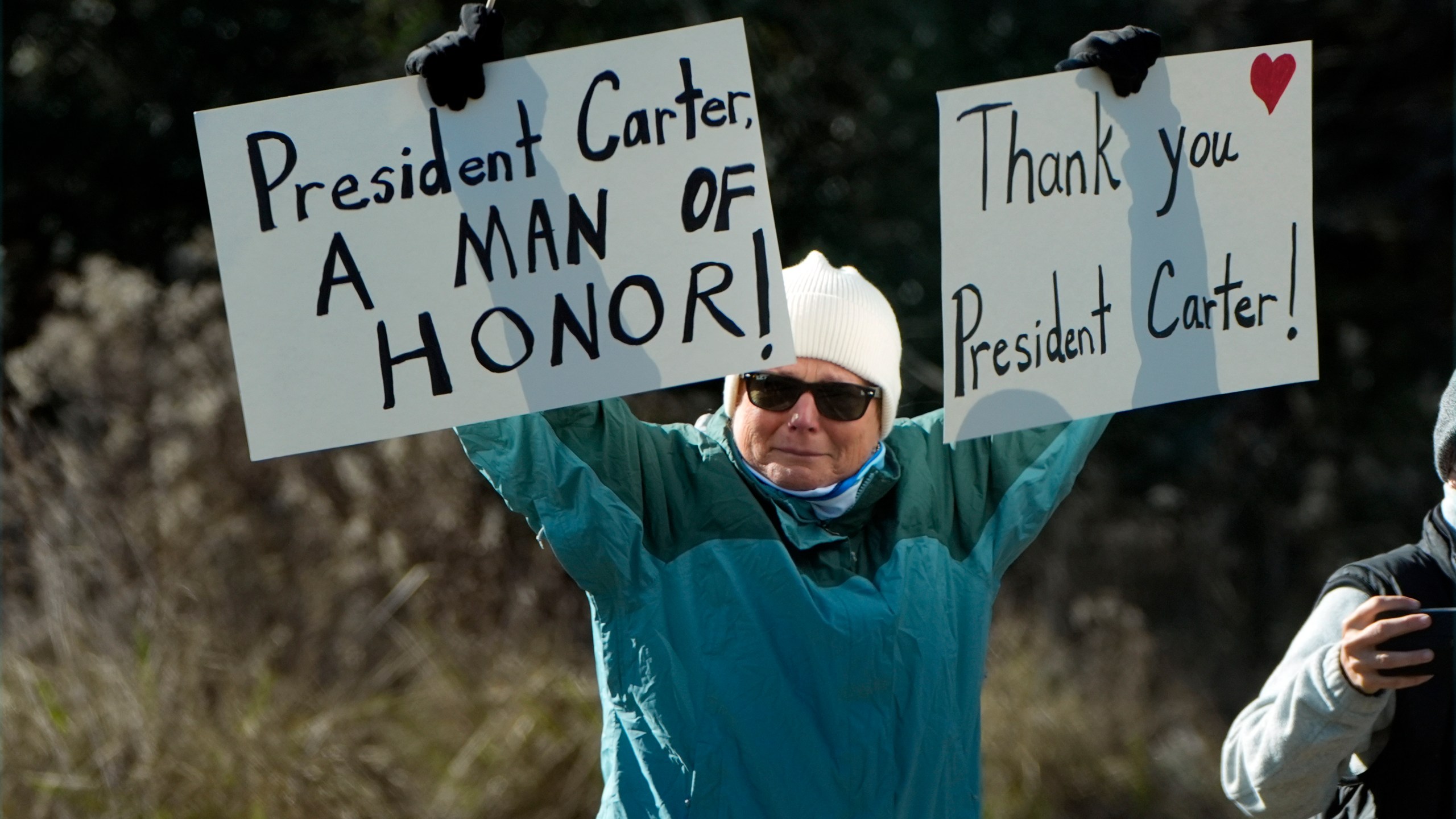 A person holds signs as the hearse containing the casket of former President Jimmy Carter, pauses at the Jimmy Carter Boyhood Farm in Archery, Ga., Saturday, Jan. 4, 2025. Carter died Dec. 29 at the age of 100. (AP Photo/Alex Brandon, Pool)