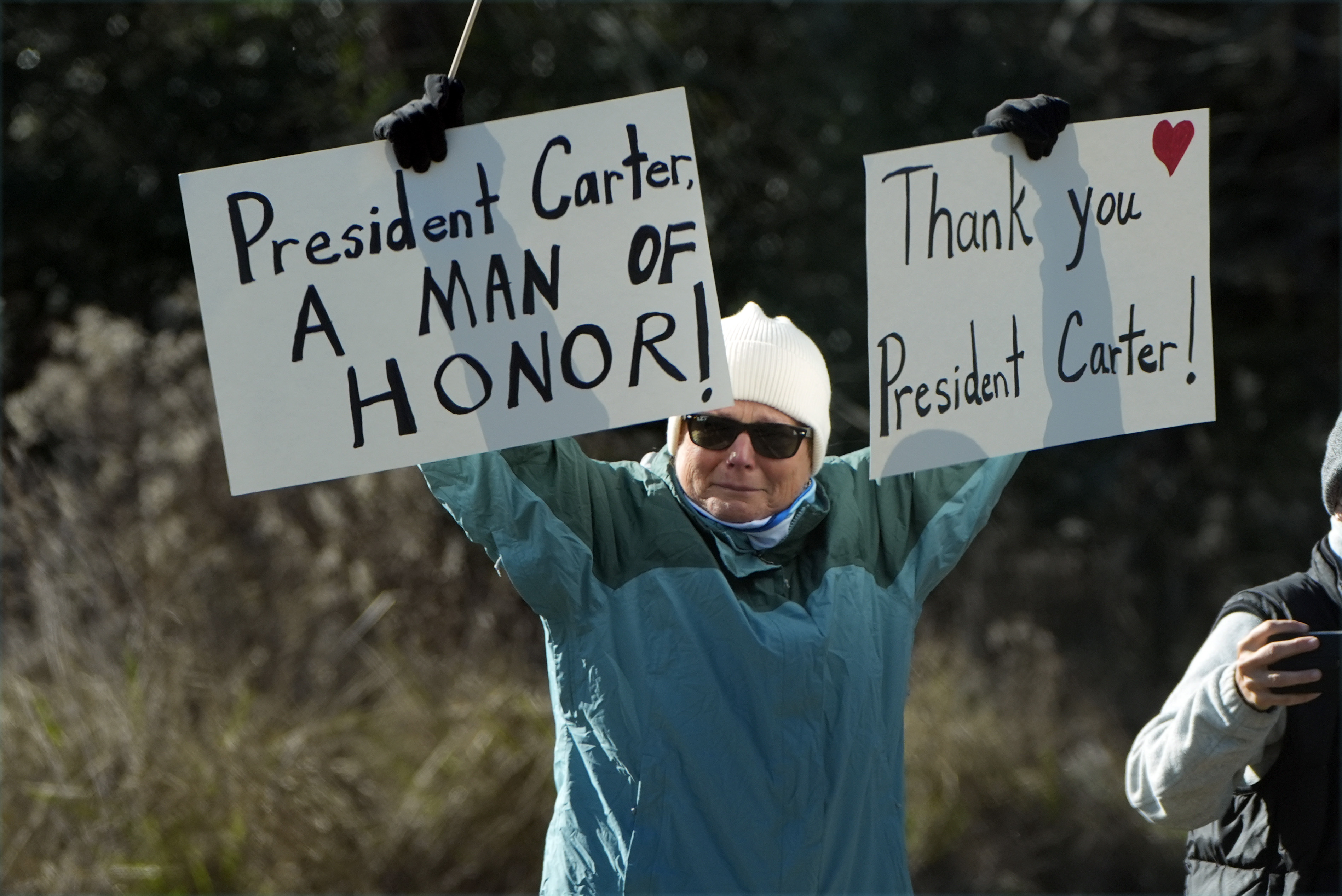 A person holds signs as the hearse containing the casket of former President Jimmy Carter, pauses at the Jimmy Carter Boyhood Farm in Archery, Ga., Saturday, Jan. 4, 2025. Carter died Dec. 29 at the age of 100. (AP Photo/Alex Brandon, Pool)