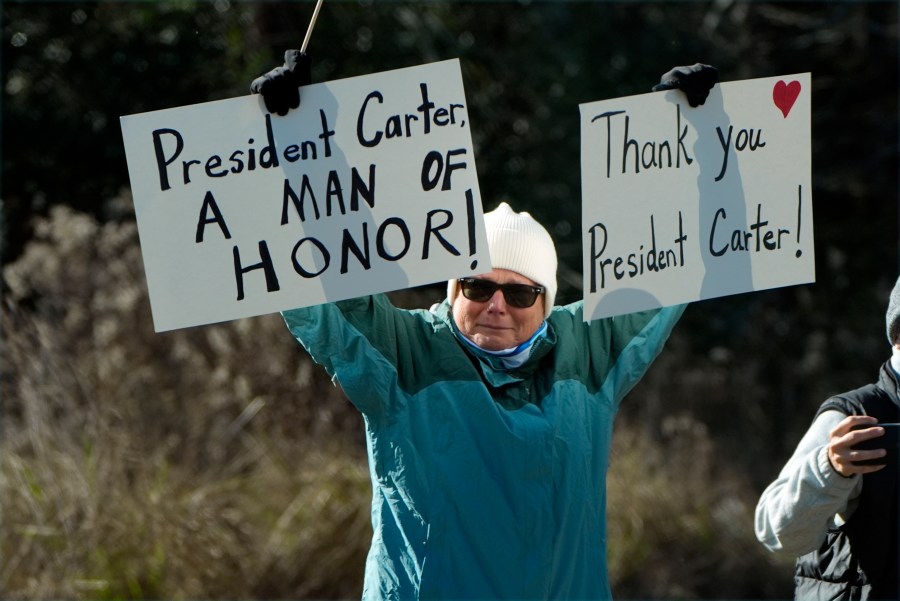 A person holds signs as the hearse containing the casket of former President Jimmy Carter, pauses at the Jimmy Carter Boyhood Farm in Archery, Ga., Saturday, Jan. 4, 2025. Carter died Dec. 29 at the age of 100. (AP Photo/Alex Brandon, Pool)