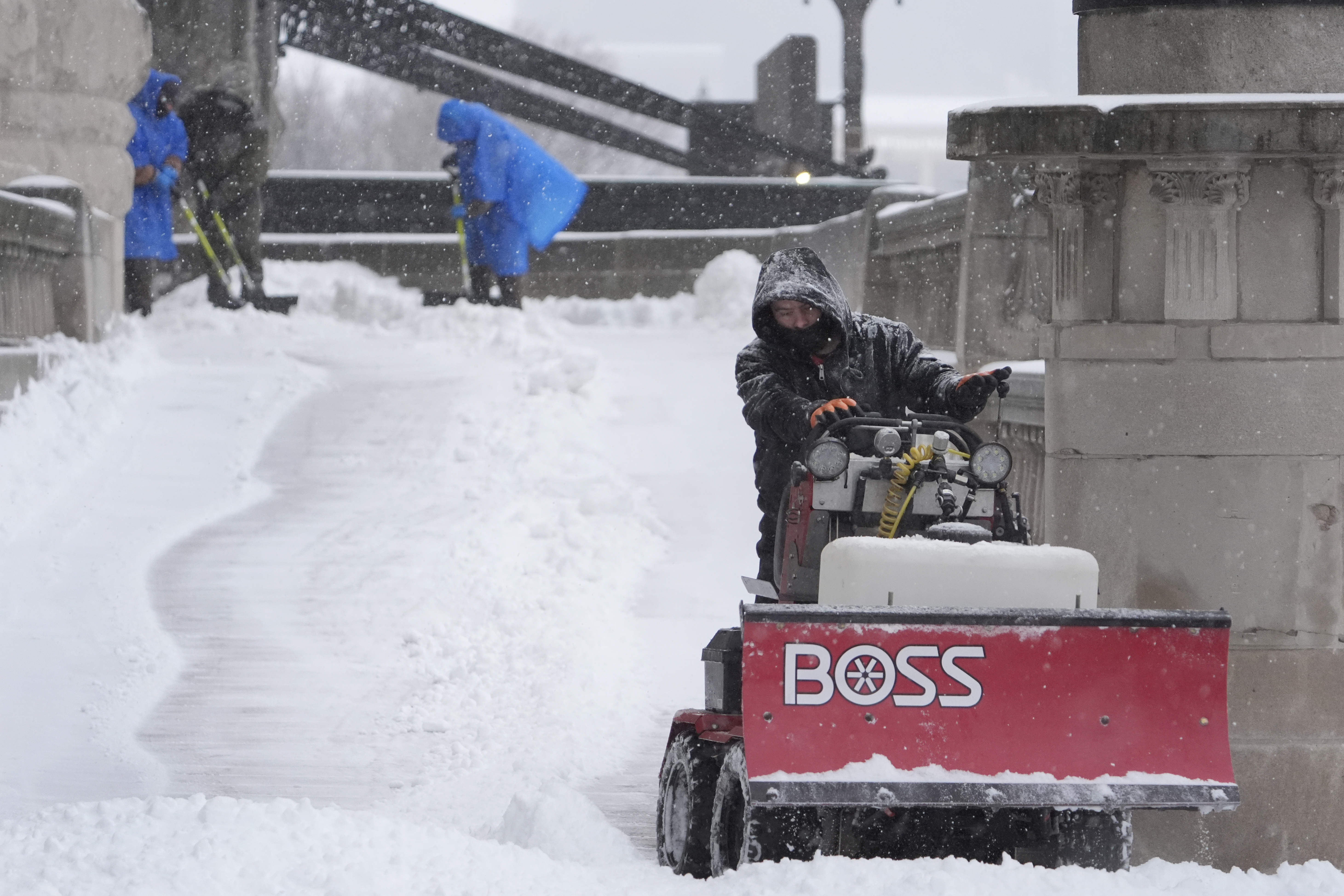 Workers clear snow from a walkway Sunday, Jan. 5, 2025, in St. Louis. (AP Photo/Jeff Roberson)