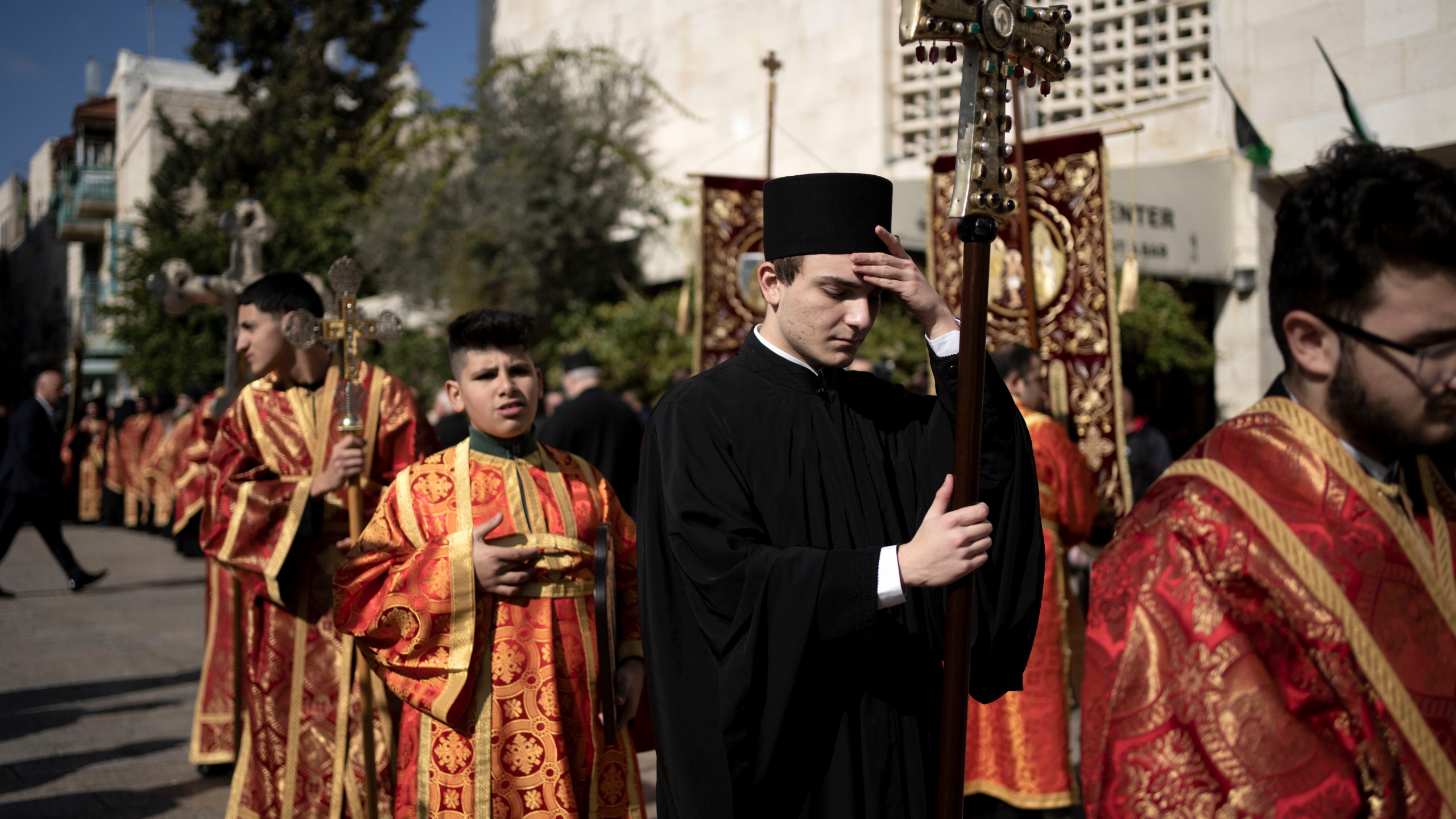 A Greek Orthodox altar boy pauses in Manger Square near the Church of the Nativity, where Christians believe Jesus Christ was born, to walk in a procession ahead of Christmas Eve mass in the West Bank city of Bethlehem, Monday, Jan. 6, 2025. (AP Photo/Maya Alleruzzo)