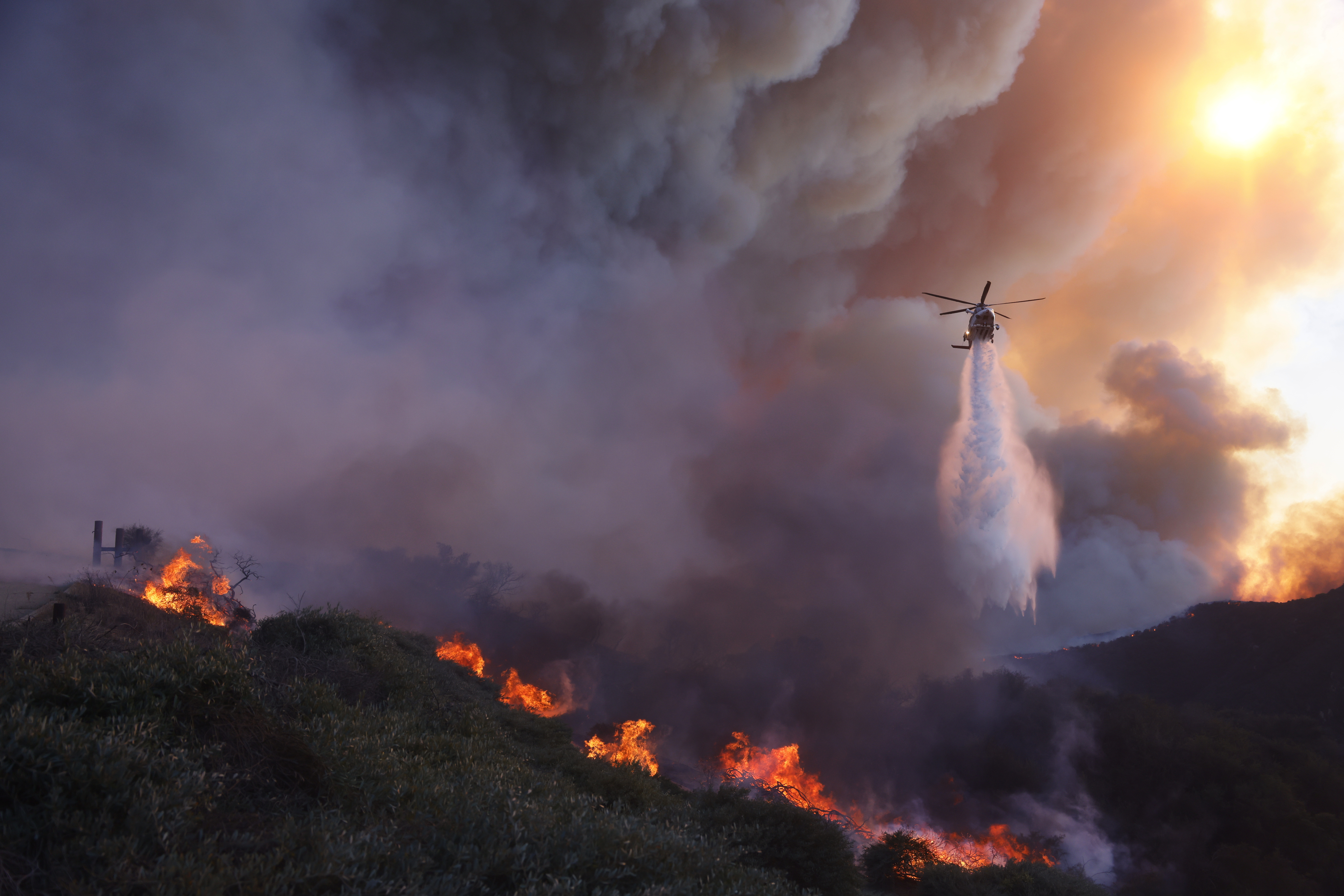 Water is dropped by helicopter on the advancing Palisades Fire in the Pacific Palisades neighborhood of Los Angeles, Tuesday, Jan. 7, 2025. (AP Photo/Etienne Laurent)