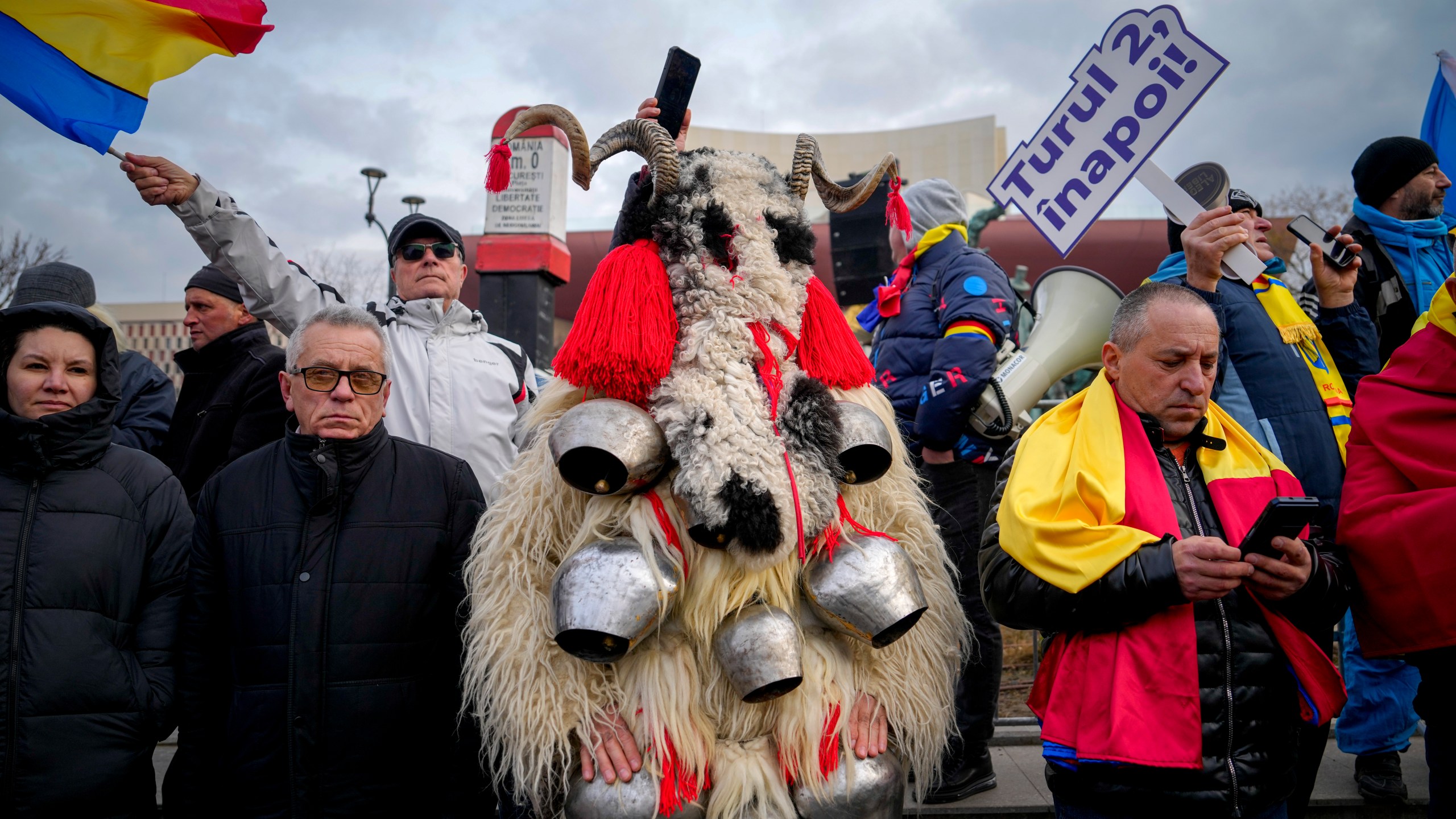 A person dressed in a costume made out of fur stands next to people waving flags and holding a banner that reads "Give us back the second round!" during a rally organized by the right wing Alliance for the Unity of Romanians (AUR), calling for free elections after Romania' s Constitutional Court annulled the first round of presidential elections last December, in Bucharest, Romania, Sunday, Jan. 12, 2025. (AP Photo/Vadim Ghirda)