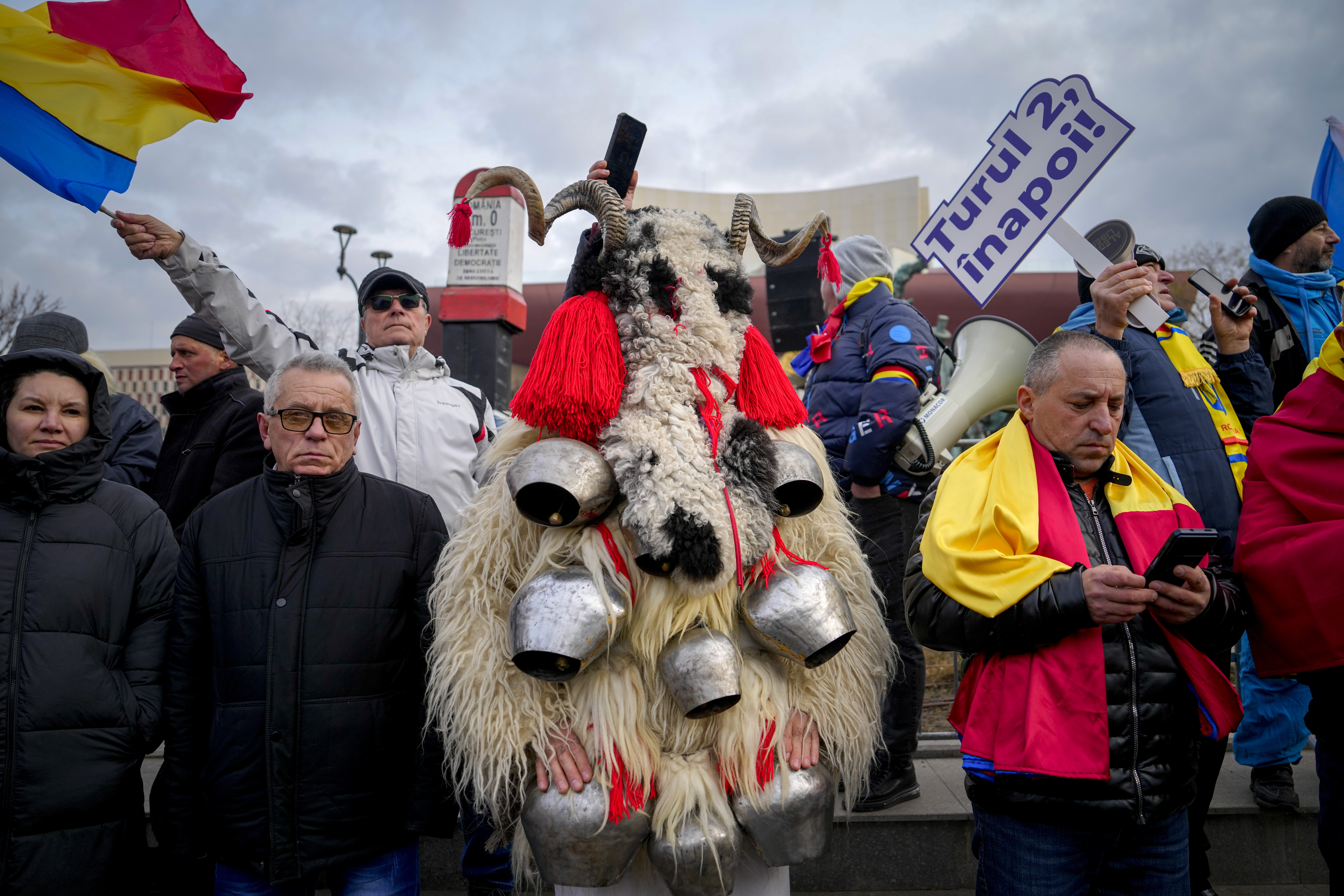 A person dressed in a costume made out of fur stands next to people waving flags and holding a banner that reads "Give us back the second round!" during a rally organized by the right wing Alliance for the Unity of Romanians (AUR), calling for free elections after Romania' s Constitutional Court annulled the first round of presidential elections last December, in Bucharest, Romania, Sunday, Jan. 12, 2025. (AP Photo/Vadim Ghirda)