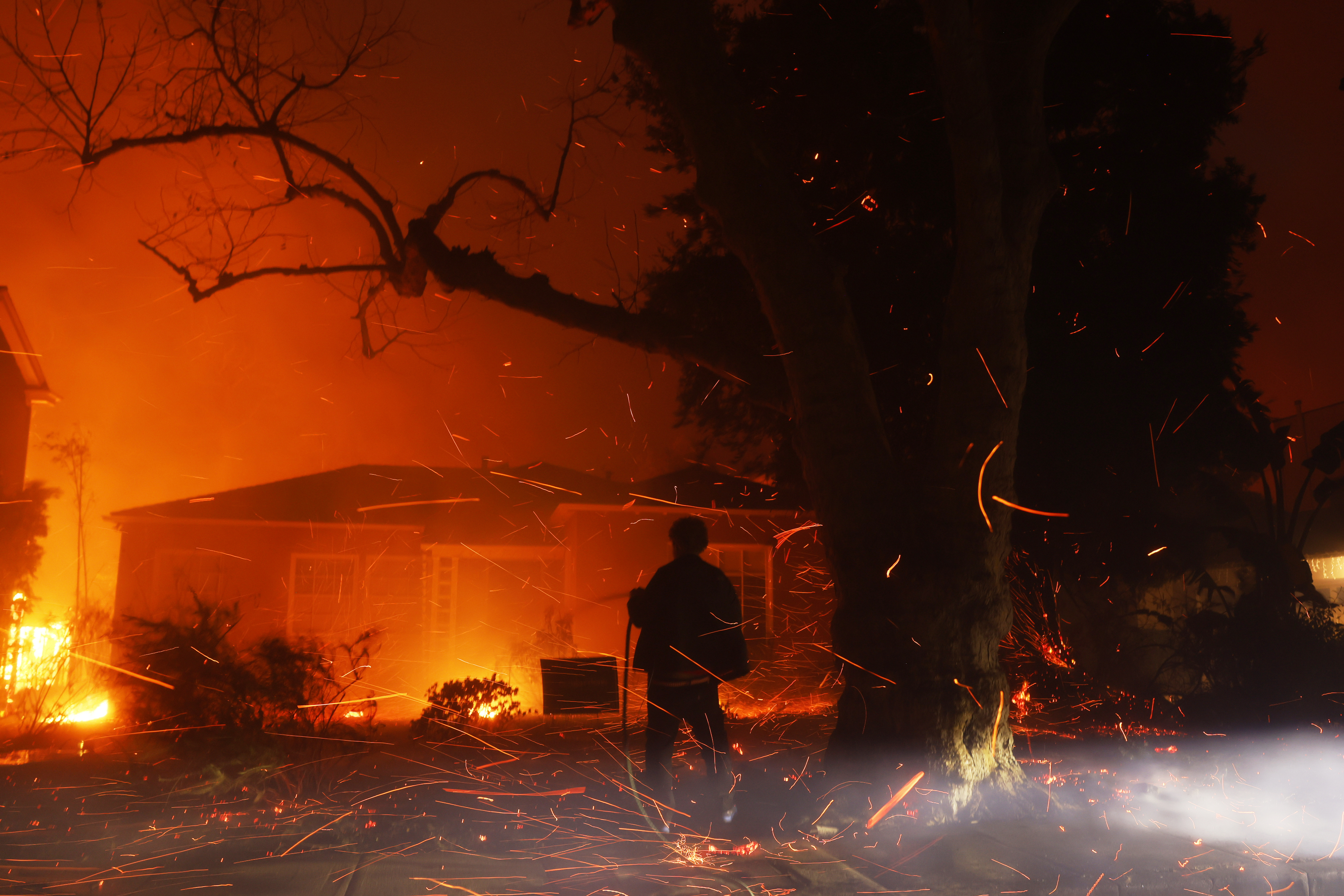 FILE - A person tries to hose down embers from the Palisades Fire in the Pacific Palisades neighborhood of Los Angeles, Jan. 7, 2025. (AP Photo/Etienne Laurent, File)