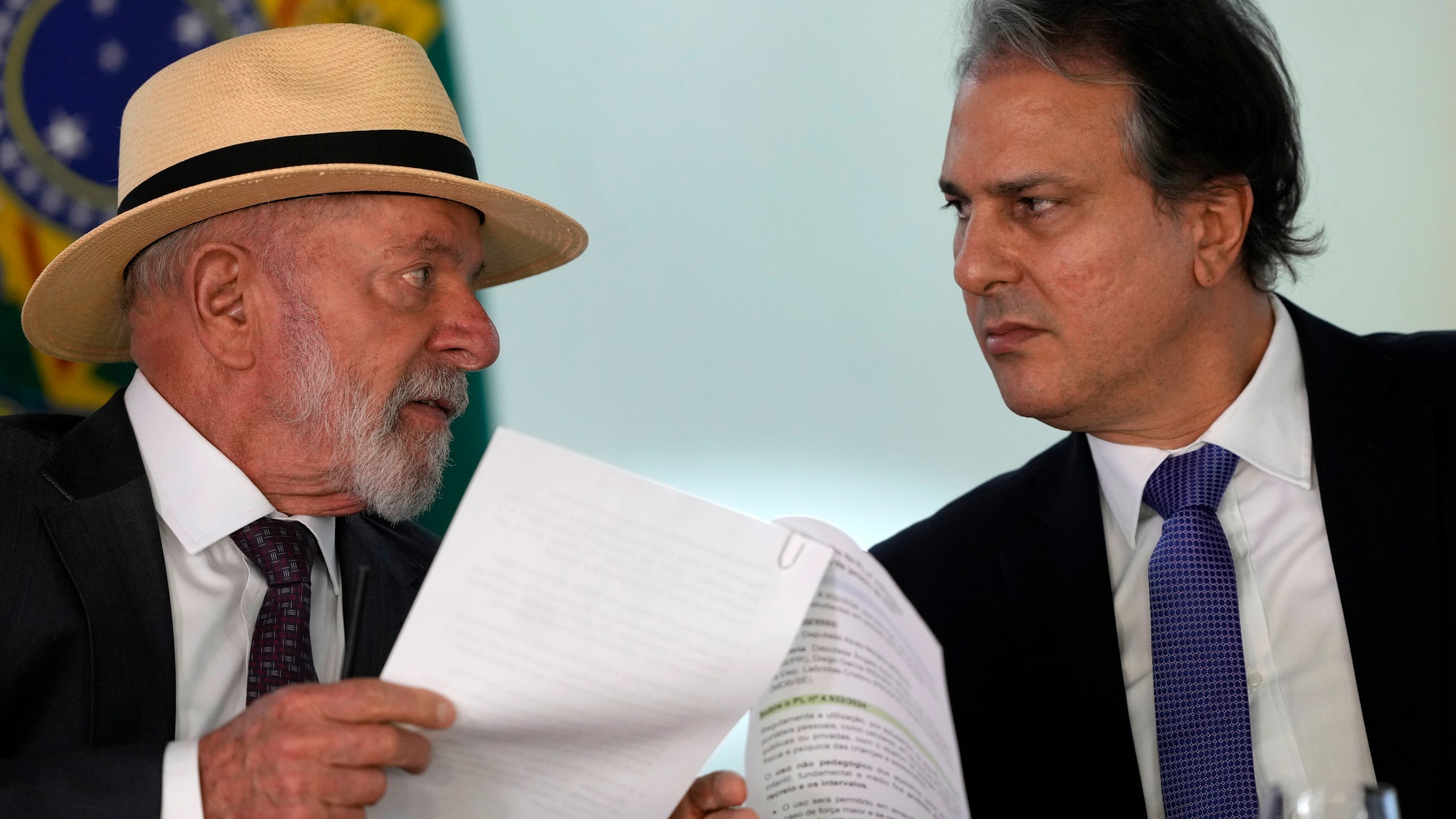 Brazil's President Luiz Inacio Lula da Silva, left, speaks with Education Minister Camilo Santana, about a bill that restricts the use of cell phones in schools nationwide, during a ceremony at the Planalto Palace, in Brasilia, Brazil, Monday, Jan. 13, 2025. (AP Photo/Eraldo Peres)