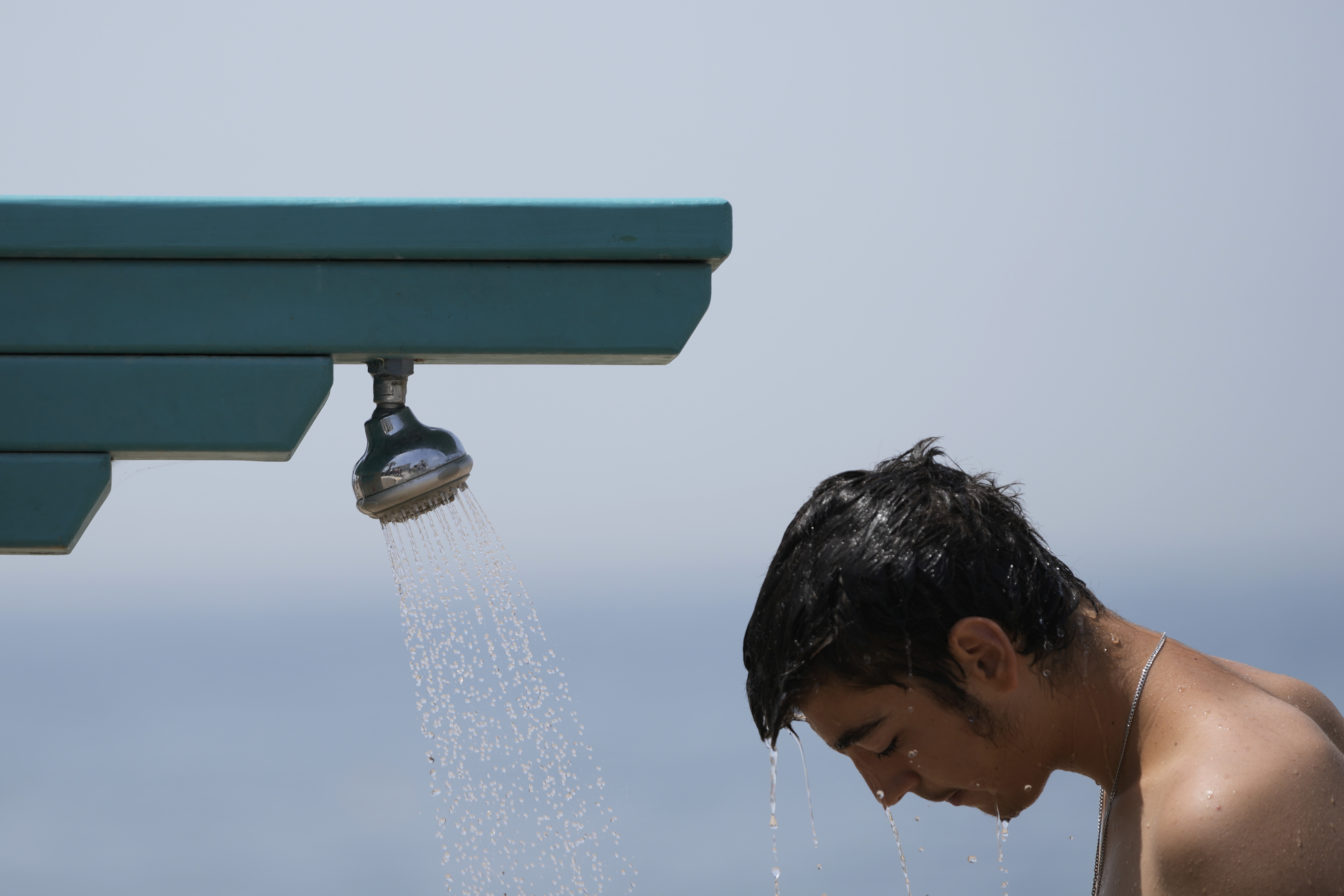 FILE - A man stands under a shower at the public beach of Paleo Faliro, in southern Athens, Greece, on June 23, 2022. (AP Photo/Thanassis Stavrakis, File)