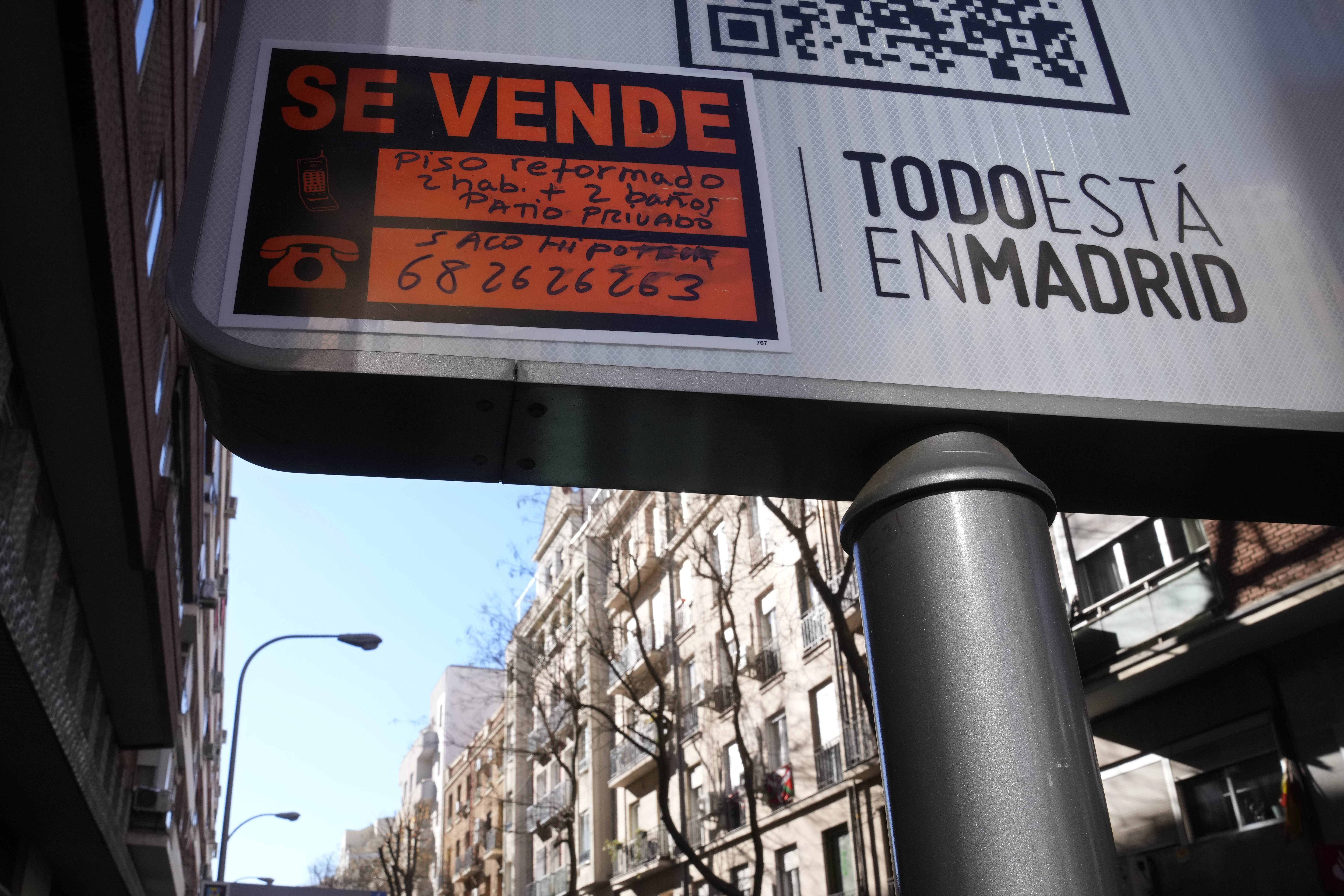 A sign advertising an apartment for sale is seen next to housing blocks in Madrid, Spain, Tuesday, Jan. 14, 2025. Sign in Spanish reads ' A renovated apartment with two rooms, two bathrooms and a private patio'. (AP Photo/Paul White)