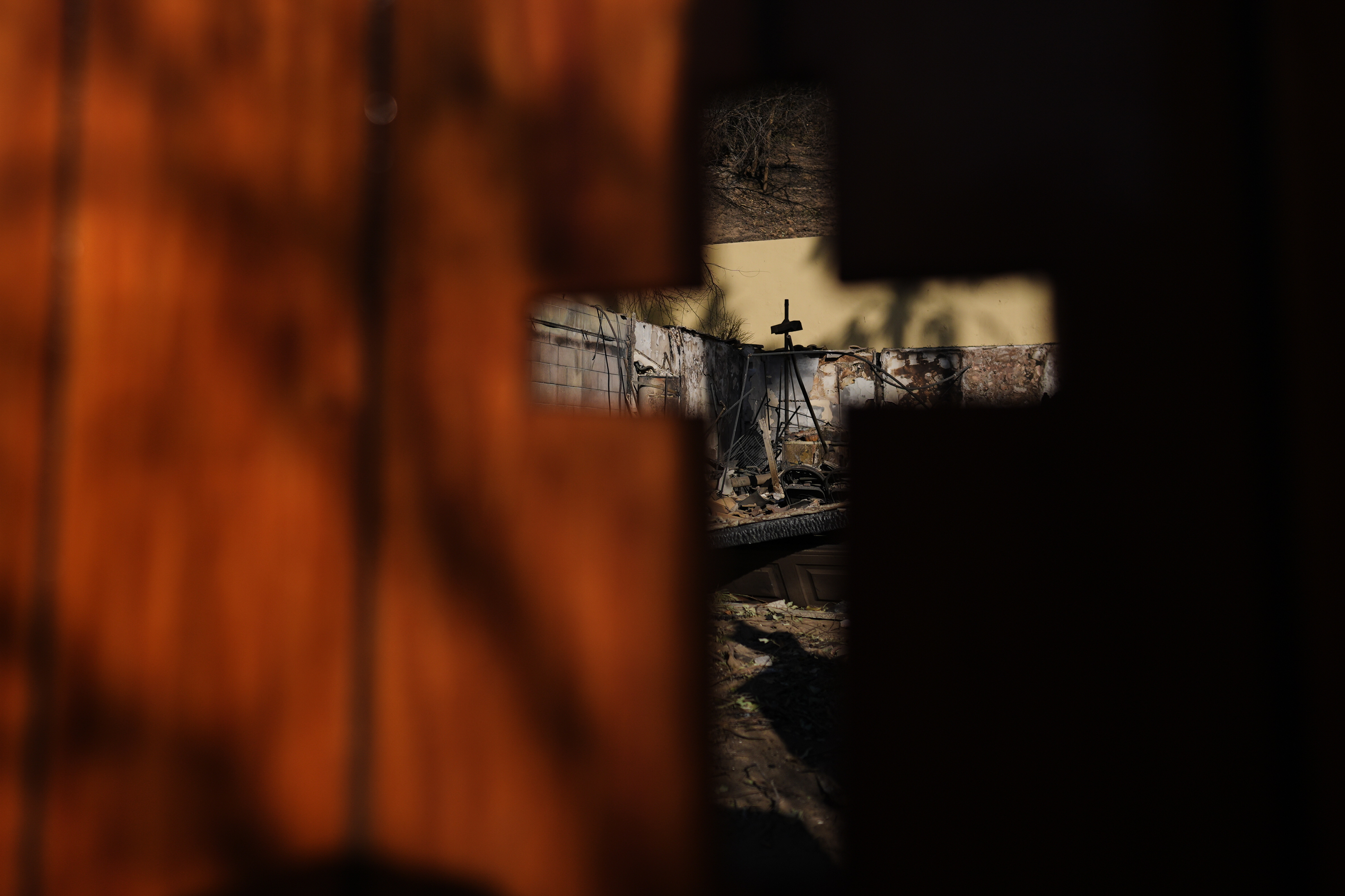 The remains of a home destroyed by the Eaton Fire are seen through a cross-shape, Thursday, Jan. 16, 2025, in Altadena, Calif. (AP Photo/Carolyn Kaster)