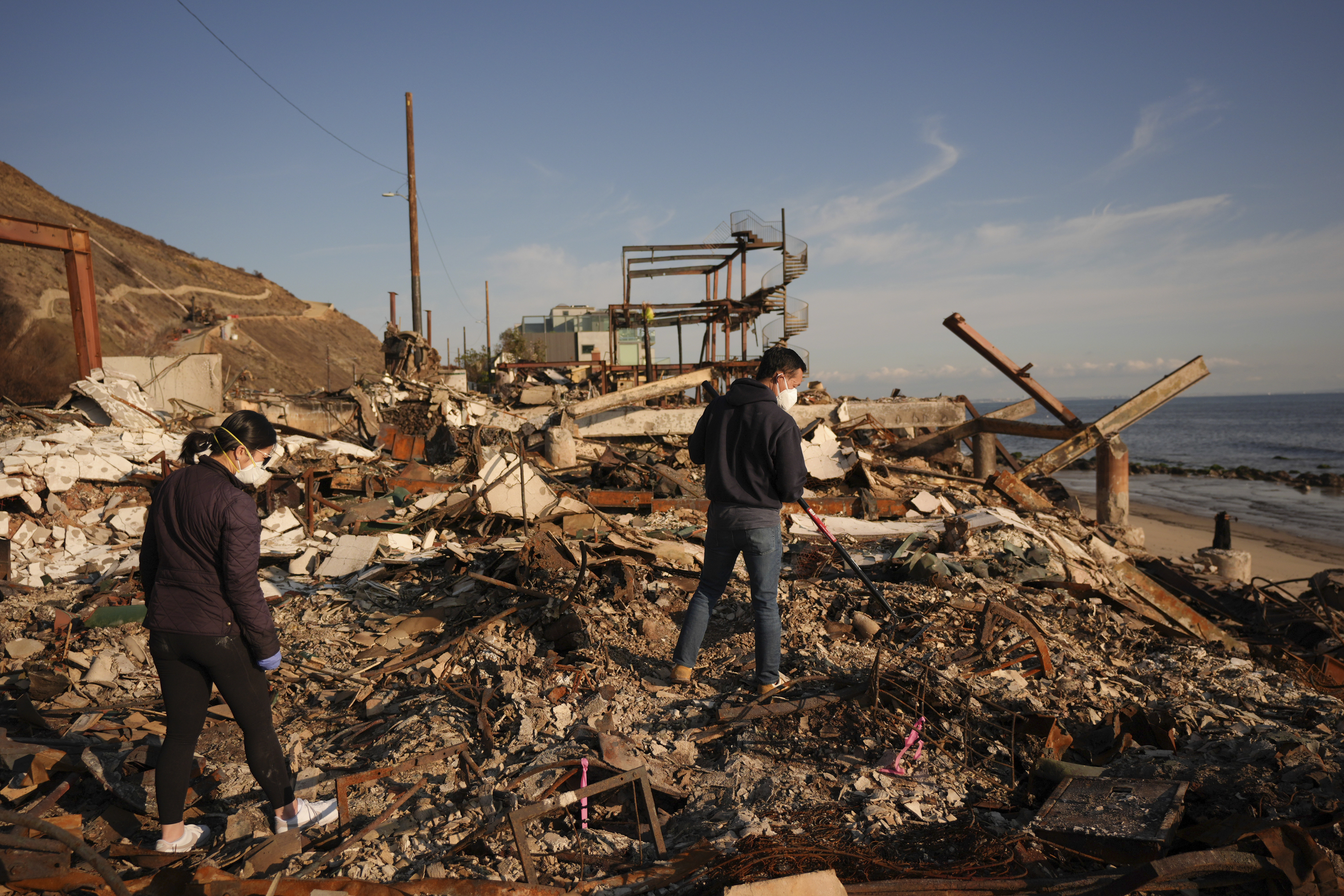 FILE - Tony Lai, center, rakes through the remains of his fire-ravaged beachfront property with his wife Everlyn in the aftermath of the Palisades Fire Tuesday, Jan. 28, 2025 in Malibu, Calif. (AP Photo/Jae C. Hong, File)