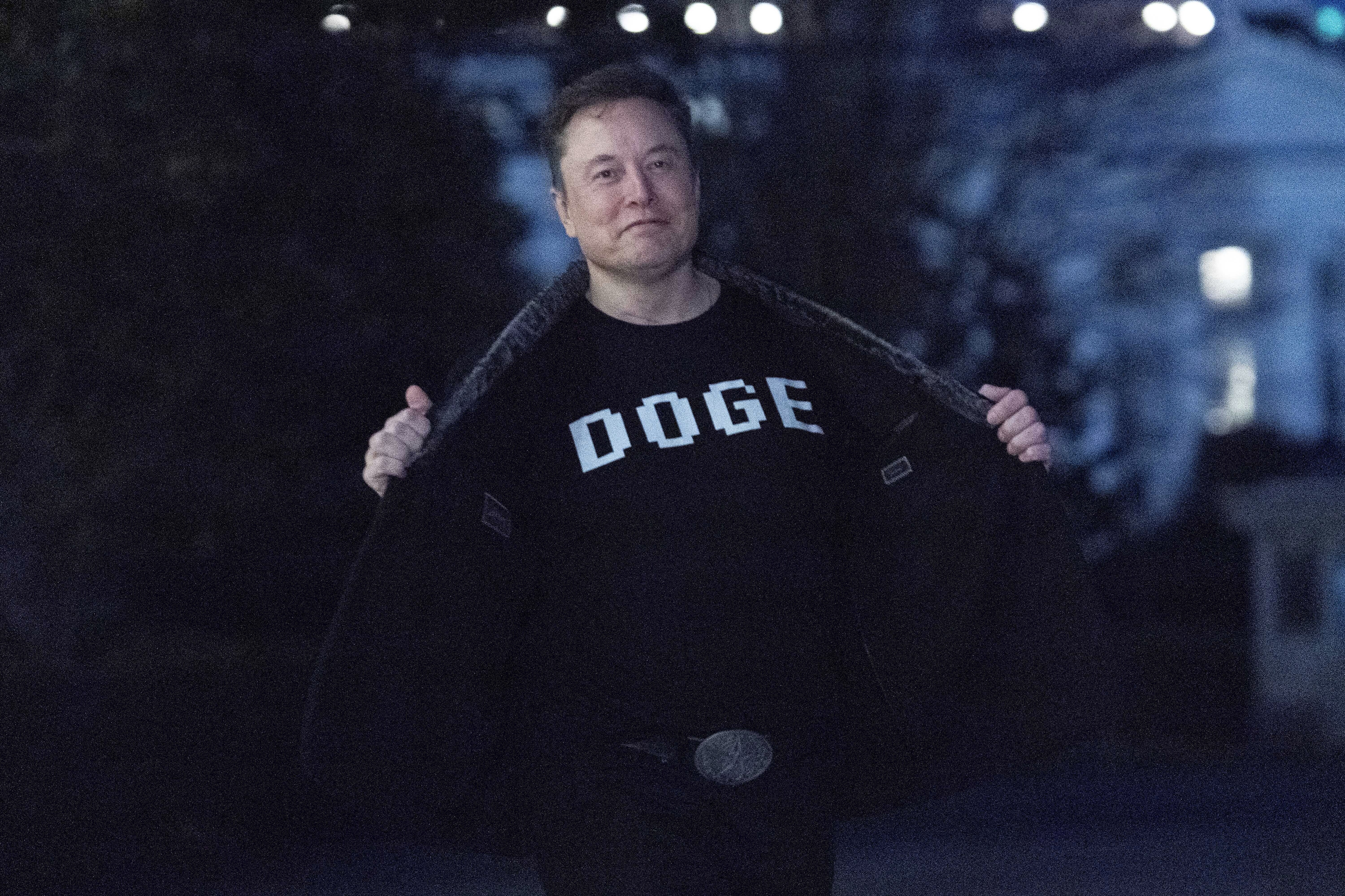 Elon Musk flashes his t-shirt that reads "DOGE" to the media as he walks on South Lawn of the White House, in Washington, Sunday, March 9, 2025. (AP Photo/Jose Luis Magana)