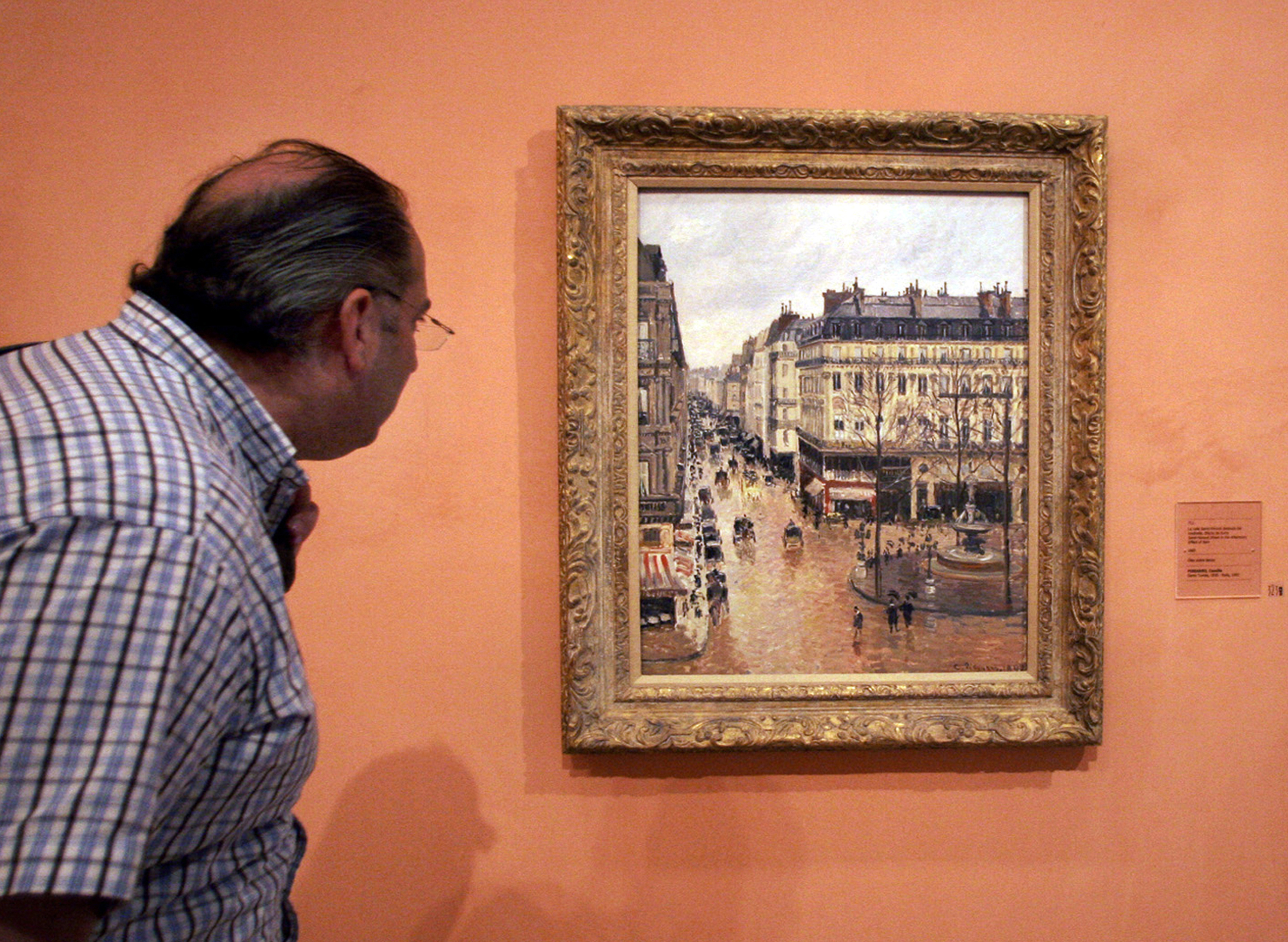 FILE - A visitor views the Impressionist painting called "Rue St.-Honore, Apres-Midi, Effet de Pluie" (“Rue Saint-Honoré in the Afternoon, Effect of Rain") painted in 1897 by Camille Pissarro, on display in the Thyssen-Bornemisza Museum May 12, 2005, in Madrid. (AP Photo/Mariana Eliano, File)