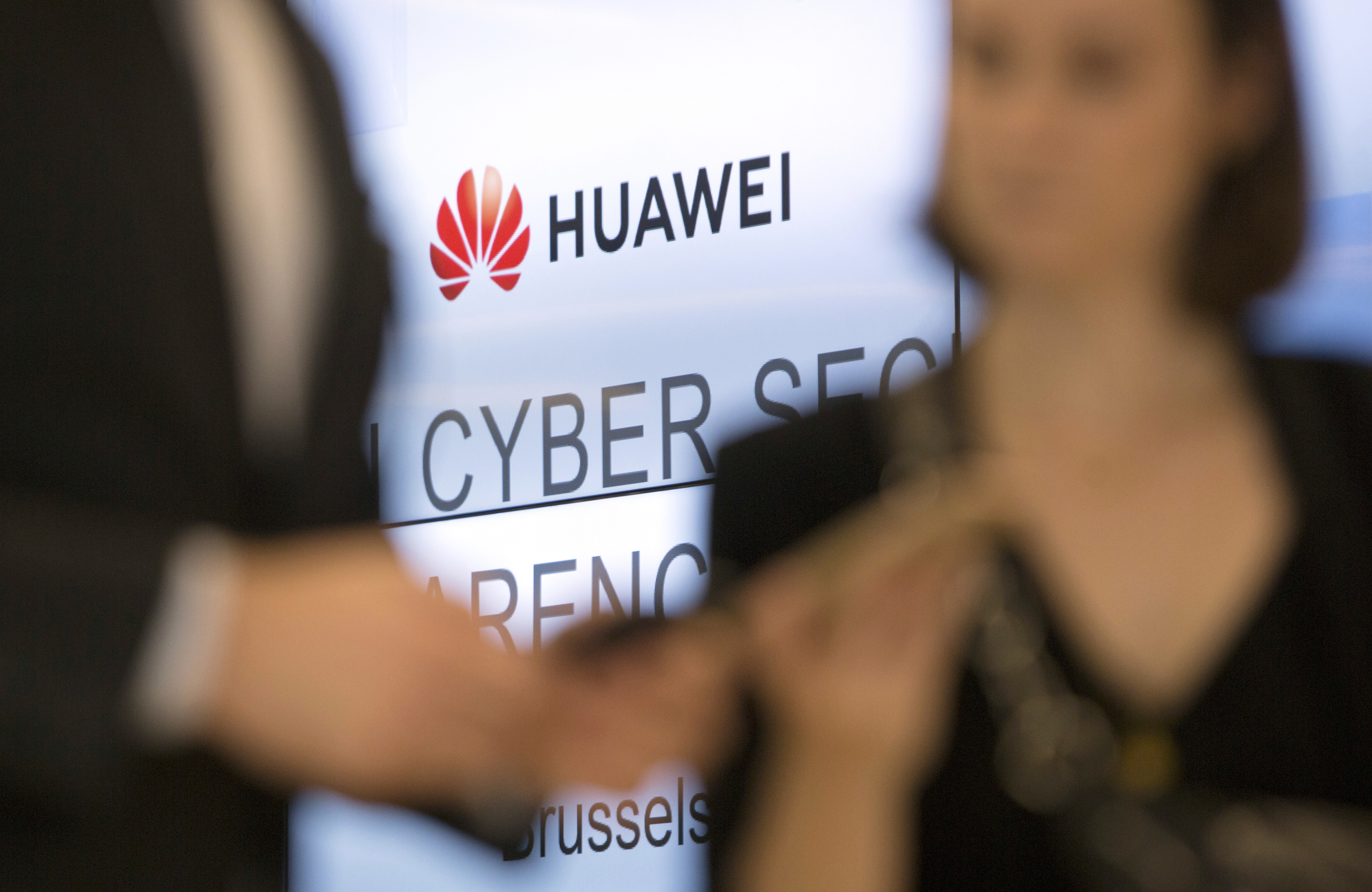 FILE - Two people look at their cellphones in front of the Huawei logo during a DigitALL lunch talk in Brussels, Tuesday, May 21, 2019. (AP Photo/Virginia Mayo, File)